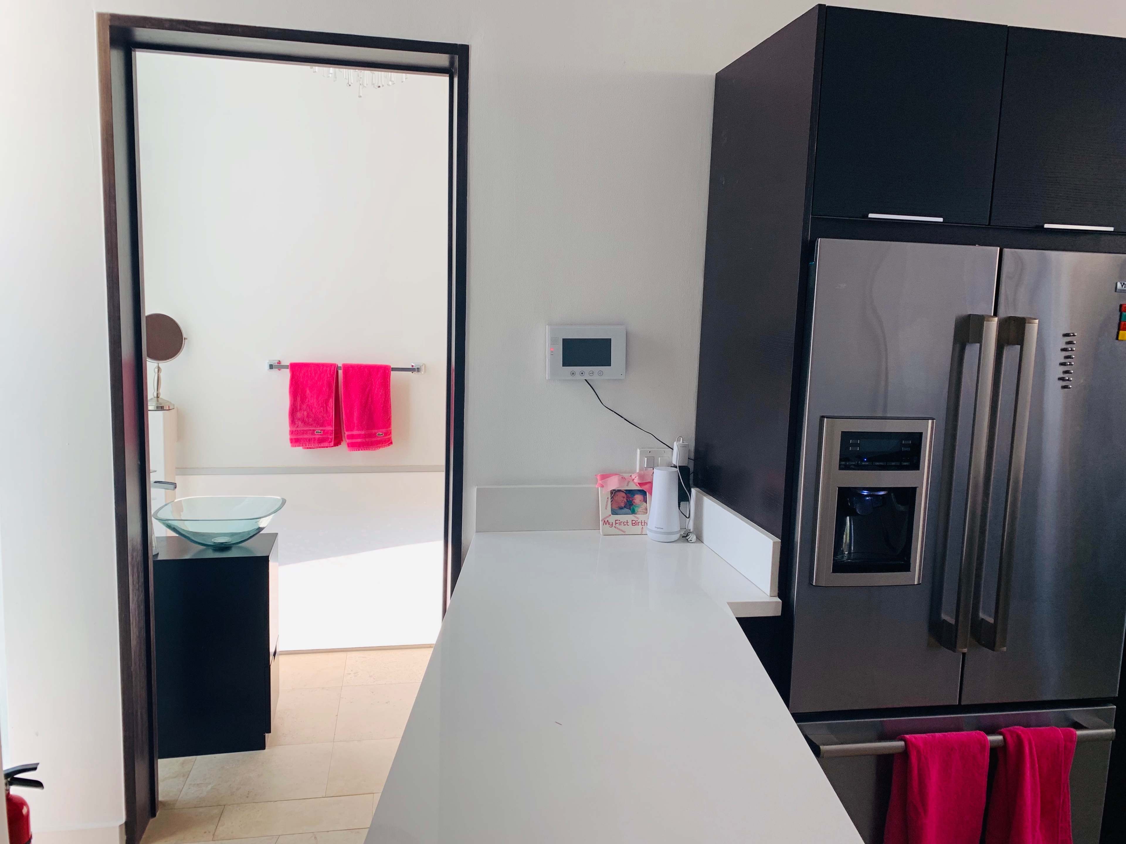 A modern kitchen with a view of a bathroom featuring pink towels and a minimalistic design.