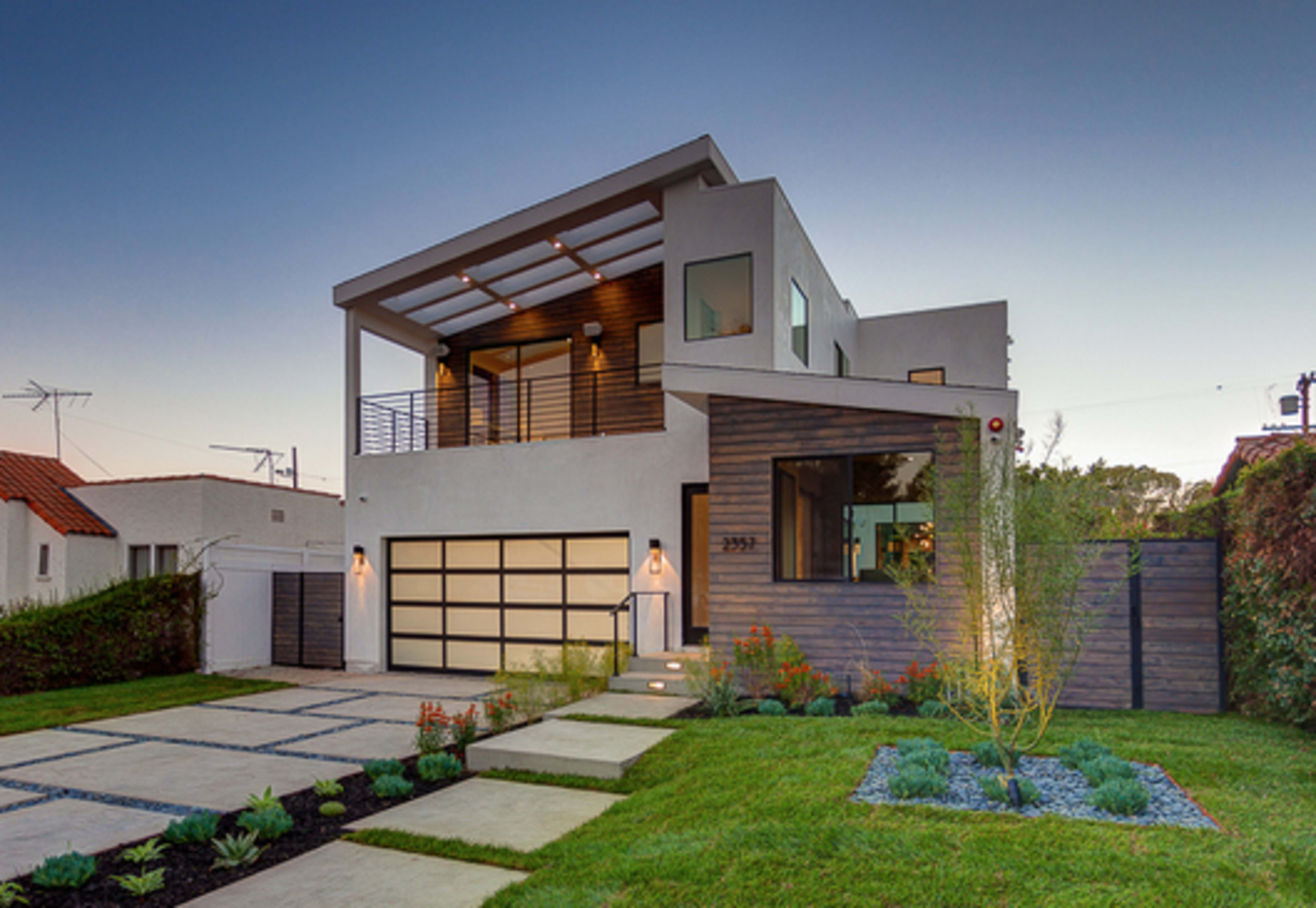 A modern two-story house with a landscaped front yard, featuring a paved pathway and a contemporary garage door.
