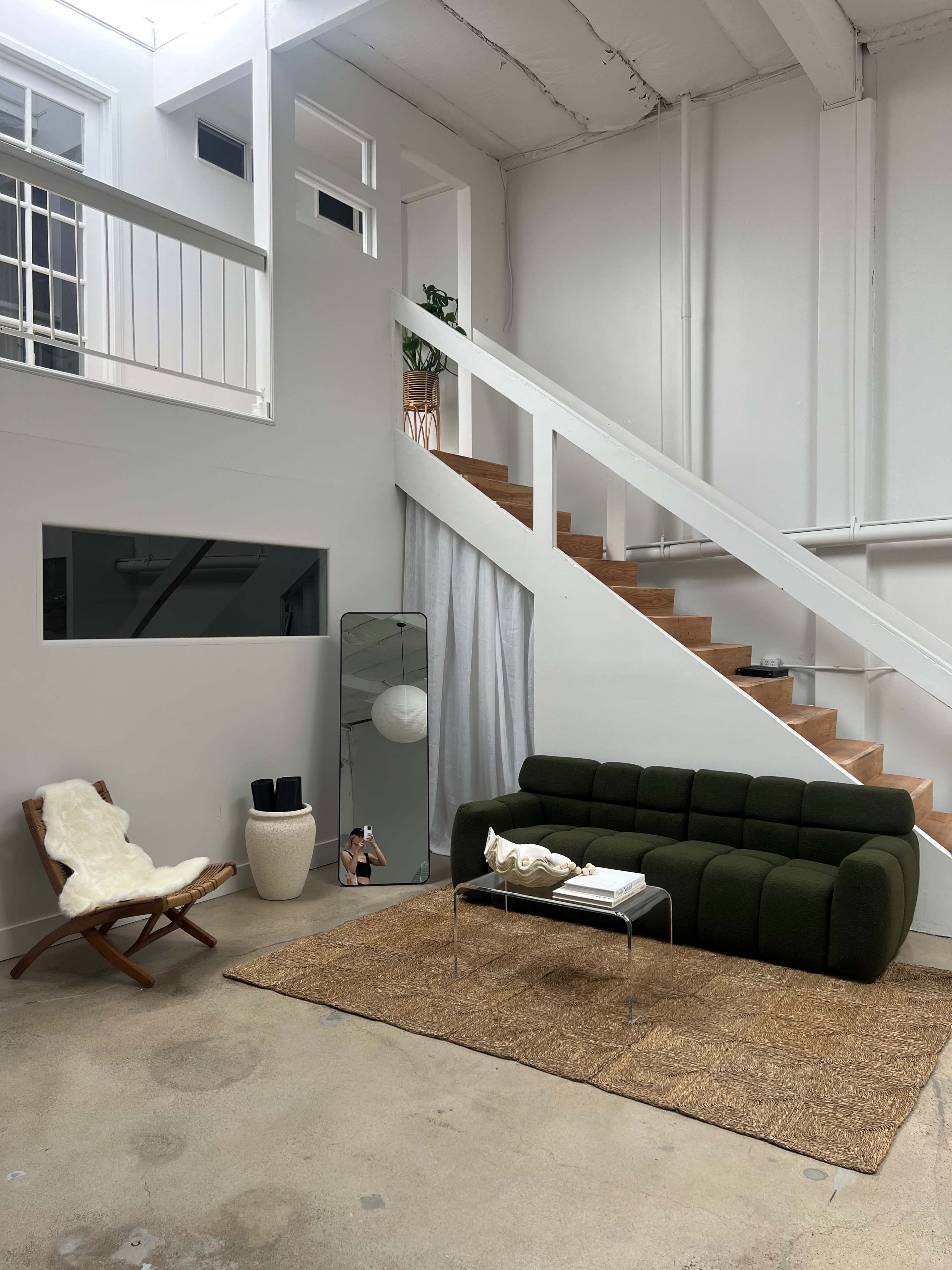 A modern living space featuring a green sofa, a woven rug, a small wooden chair, and a staircase leading to an upper level.