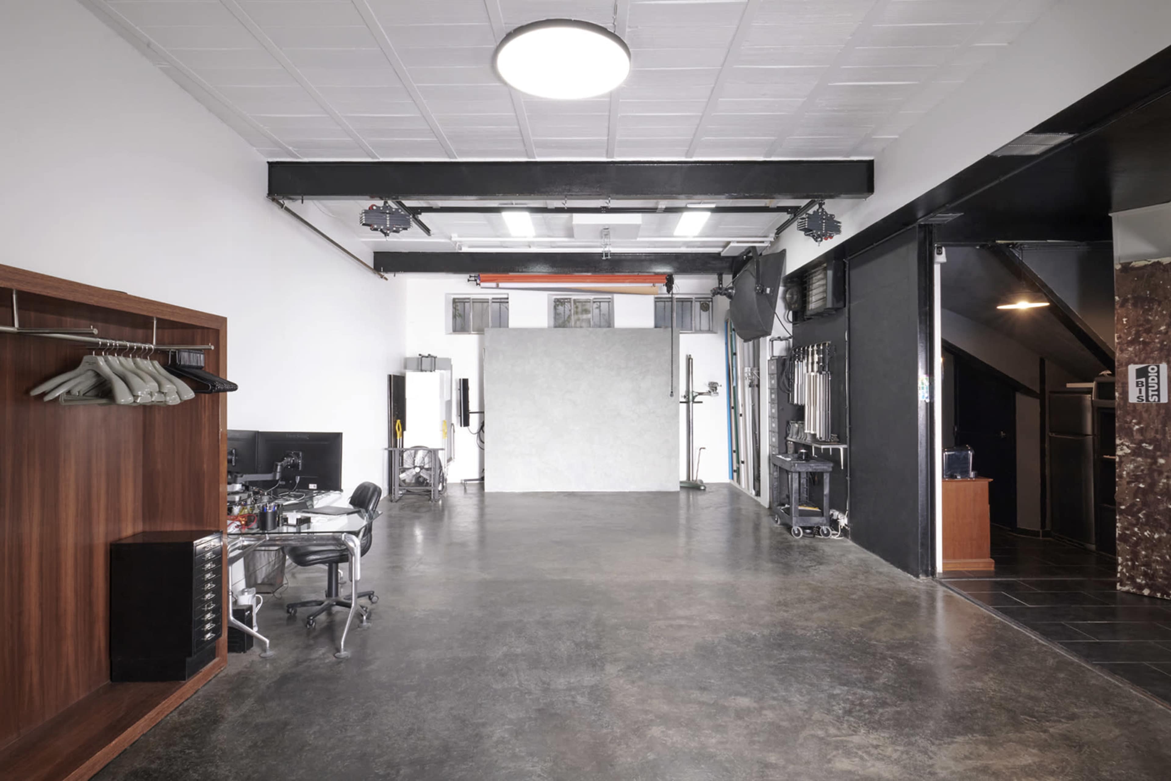A spacious, well-lit studio with a gray backdrop, a black office chair, and a clothing rack against one wall.