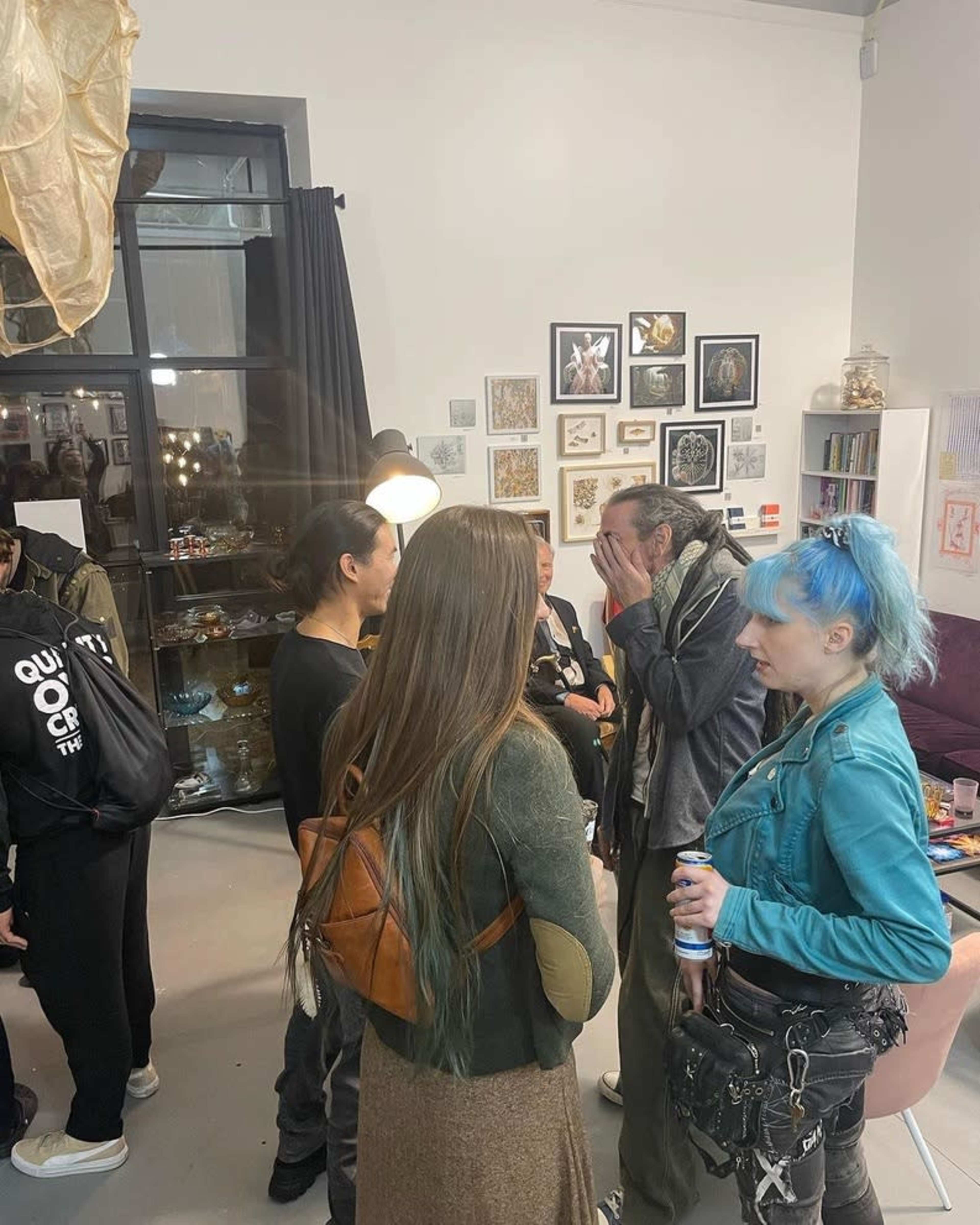 A group of people engages in conversation in an art gallery filled with various artworks on the walls.