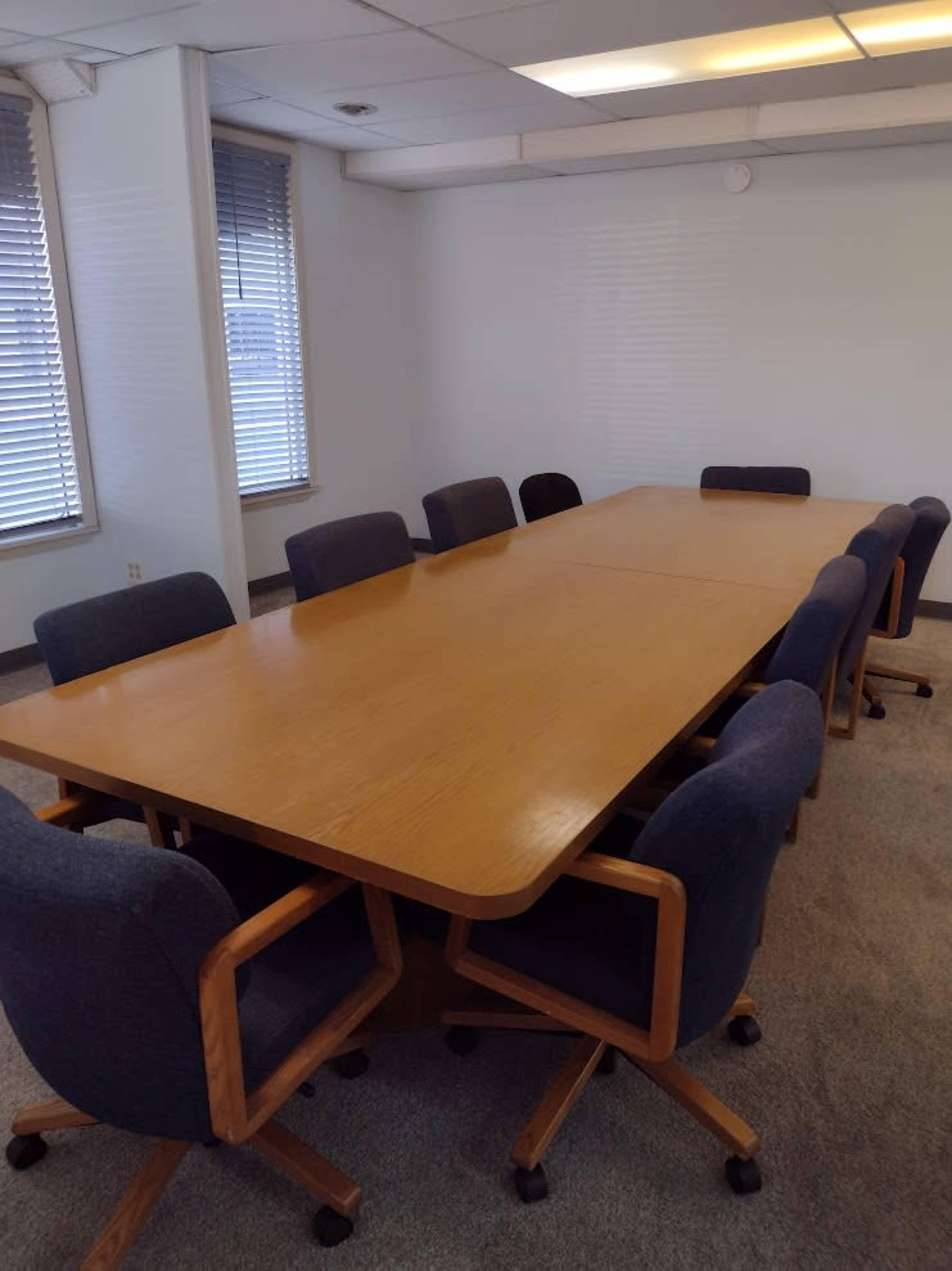 A large, rectangular conference table with eight chairs surrounds it, set in a well-lit room with windows.