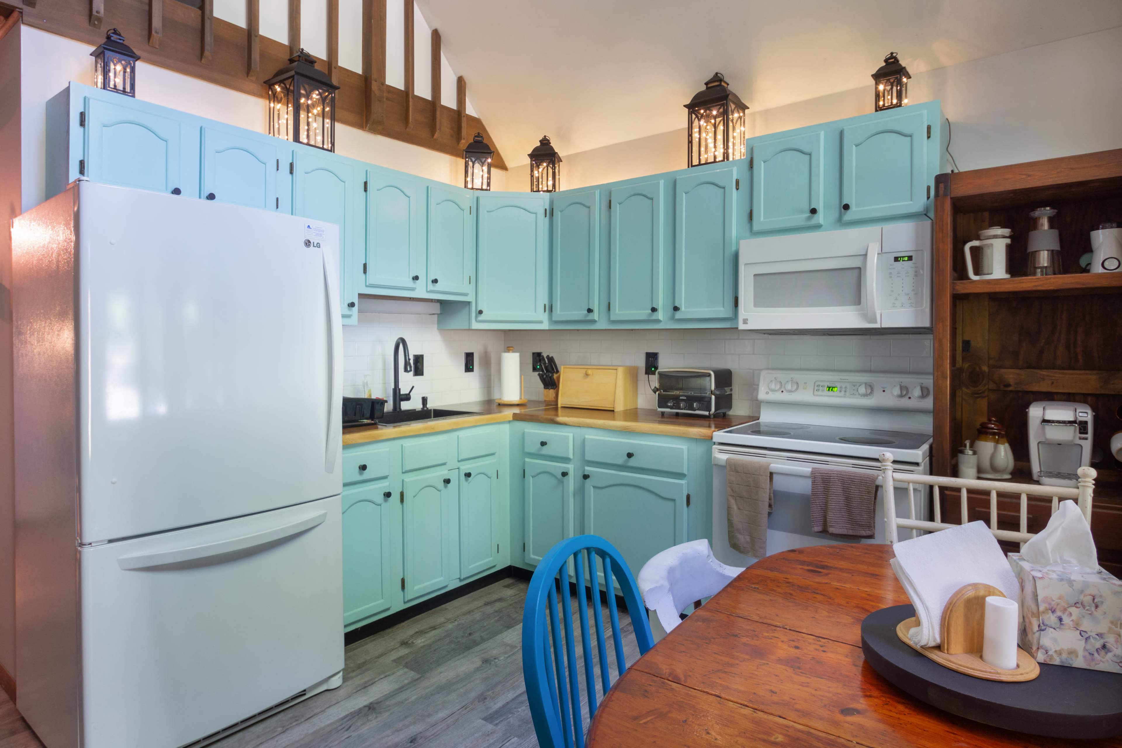 The image shows a kitchen with turquoise cabinets, a white refrigerator, a microwave, a stove, and a dining table with blue chairs.