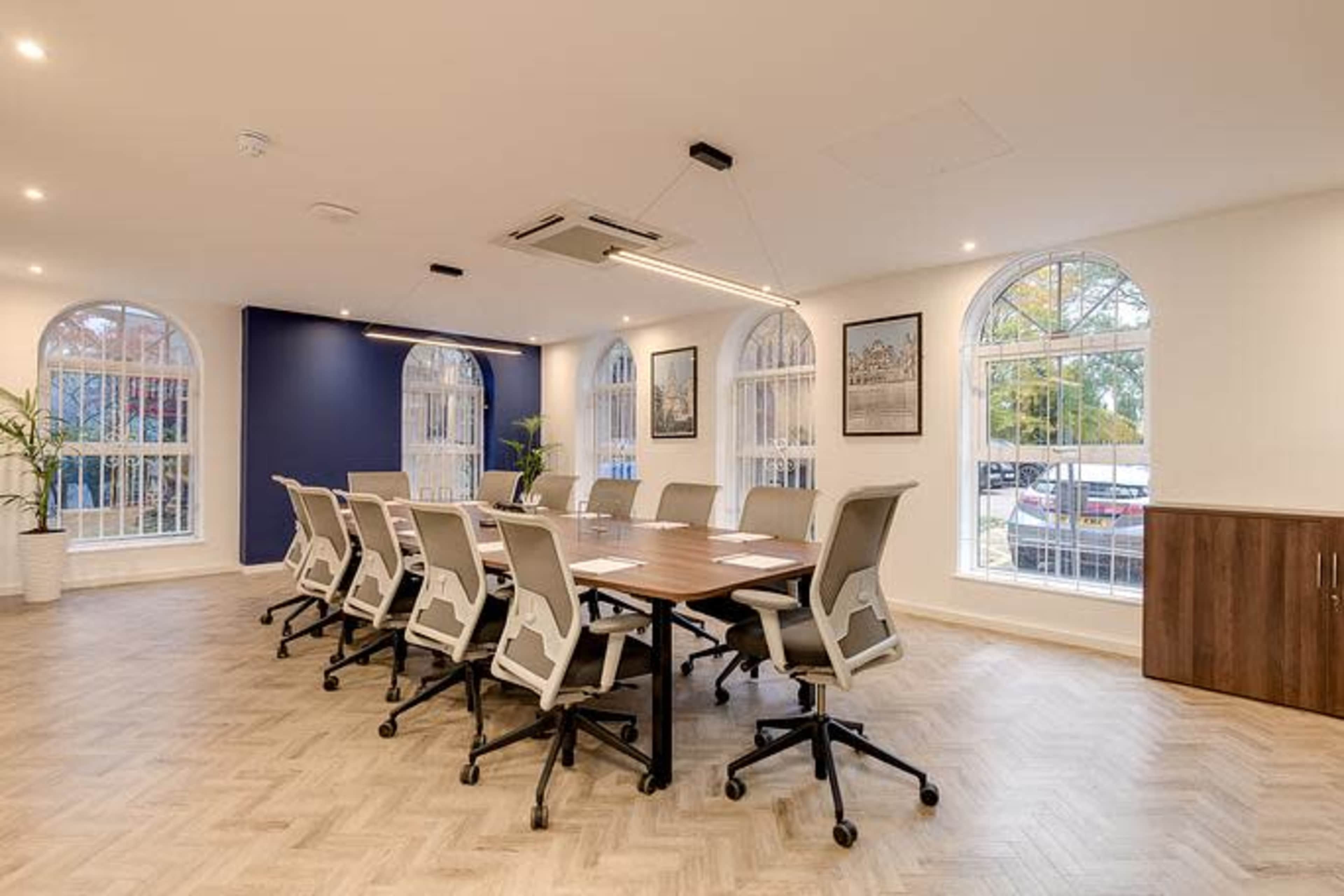 A modern conference room features a long wooden table surrounded by ergonomic chairs and large arched windows that let in natural light.