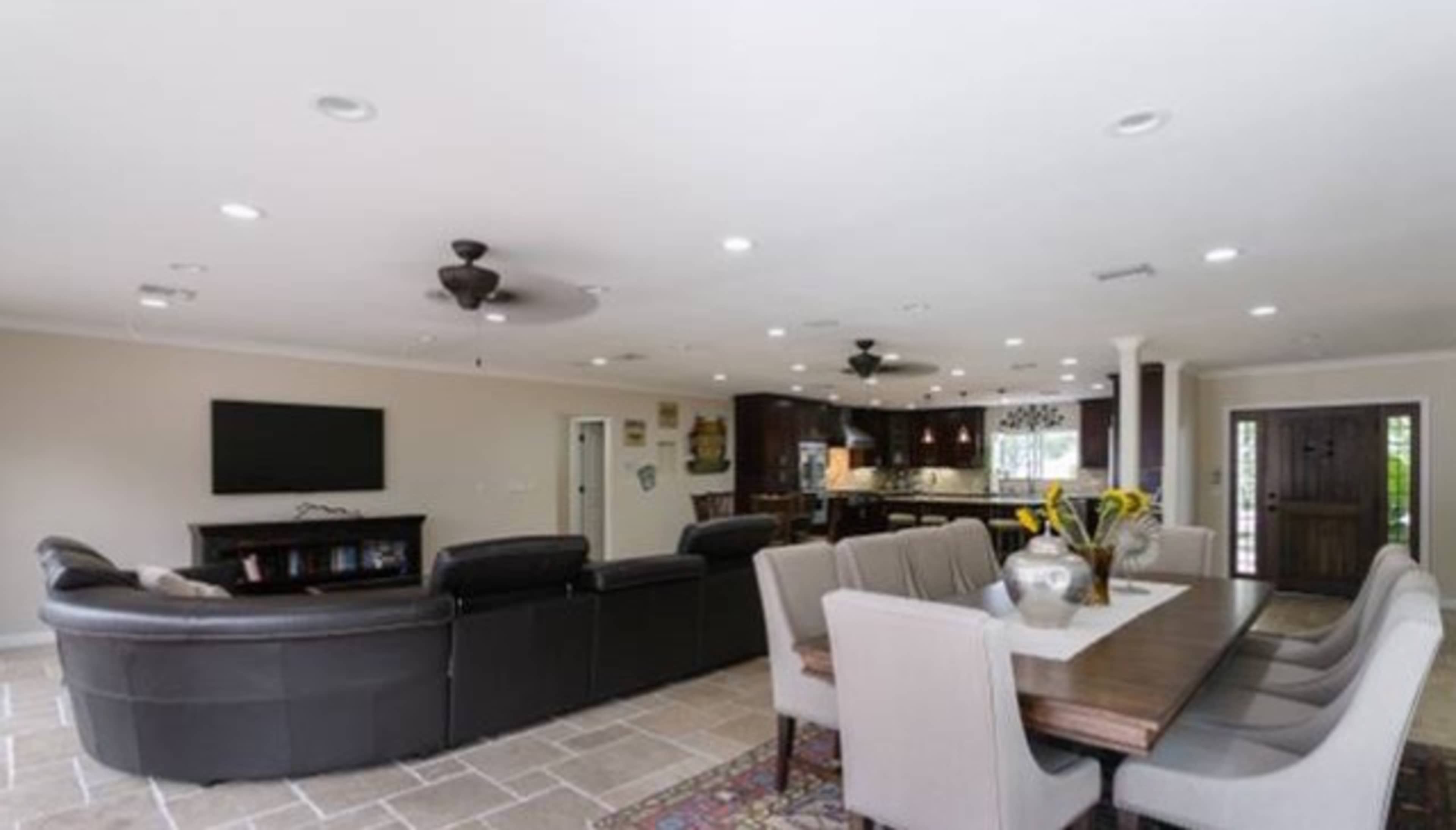 The image shows a spacious living area with a sectional sofa, a dining table, and a modern kitchen in the background.