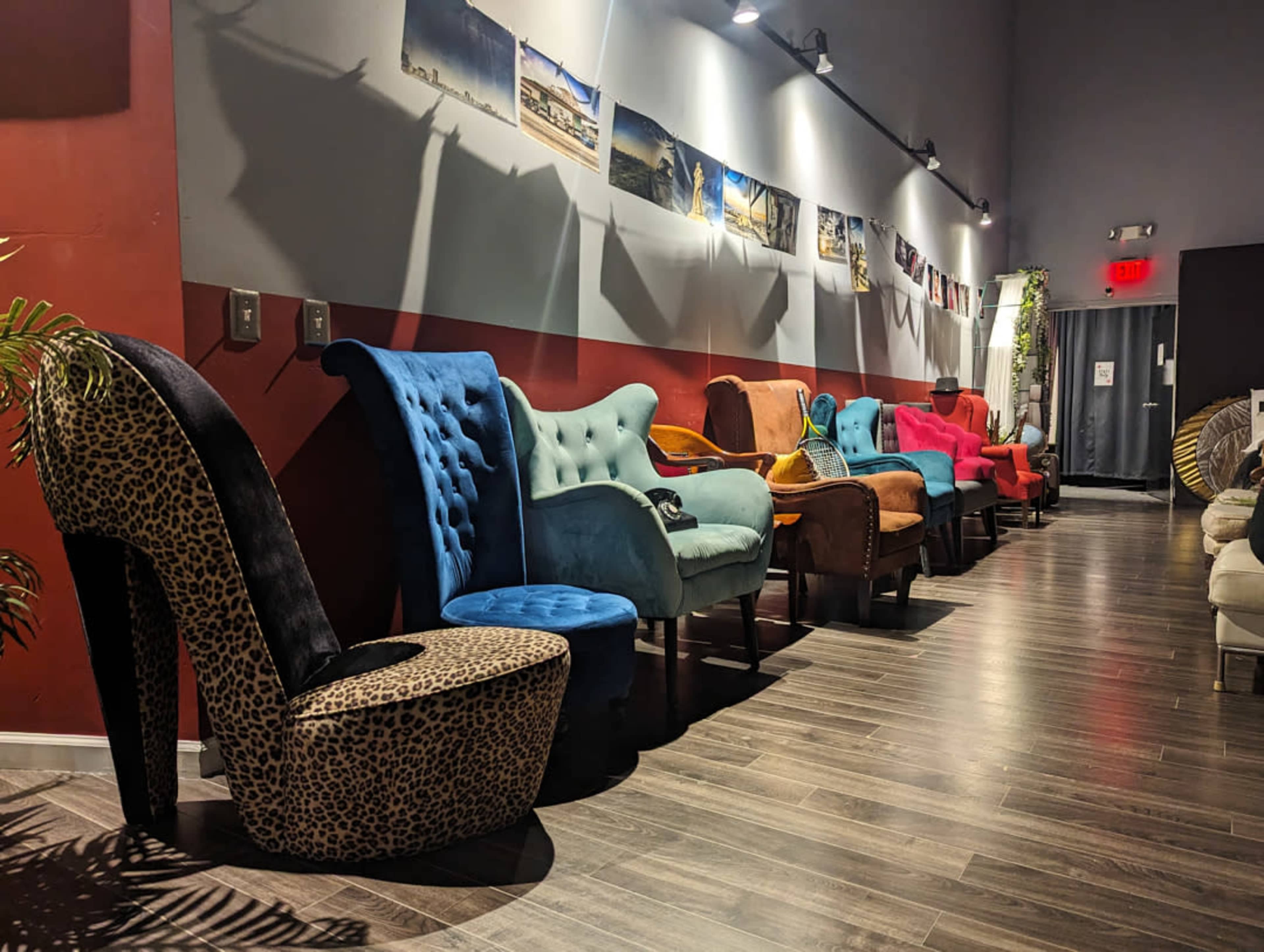 A row of uniquely designed upholstered chairs in various colors and patterns, lined along a wall with framed photographs above them.