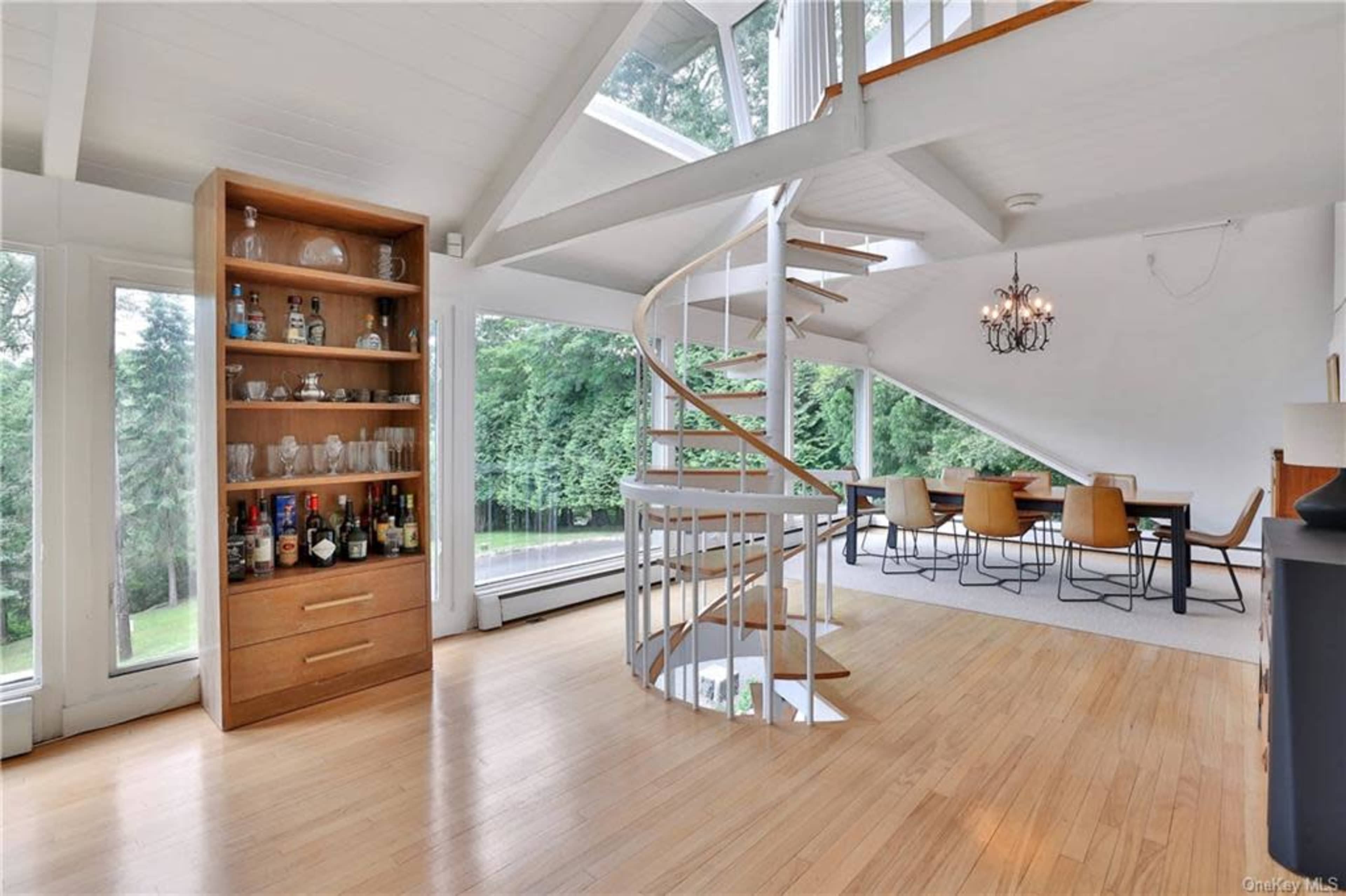 A modern interior with a spiral staircase, a wooden cabinet with glassware, and a dining area featuring a large table surrounded by chairs.