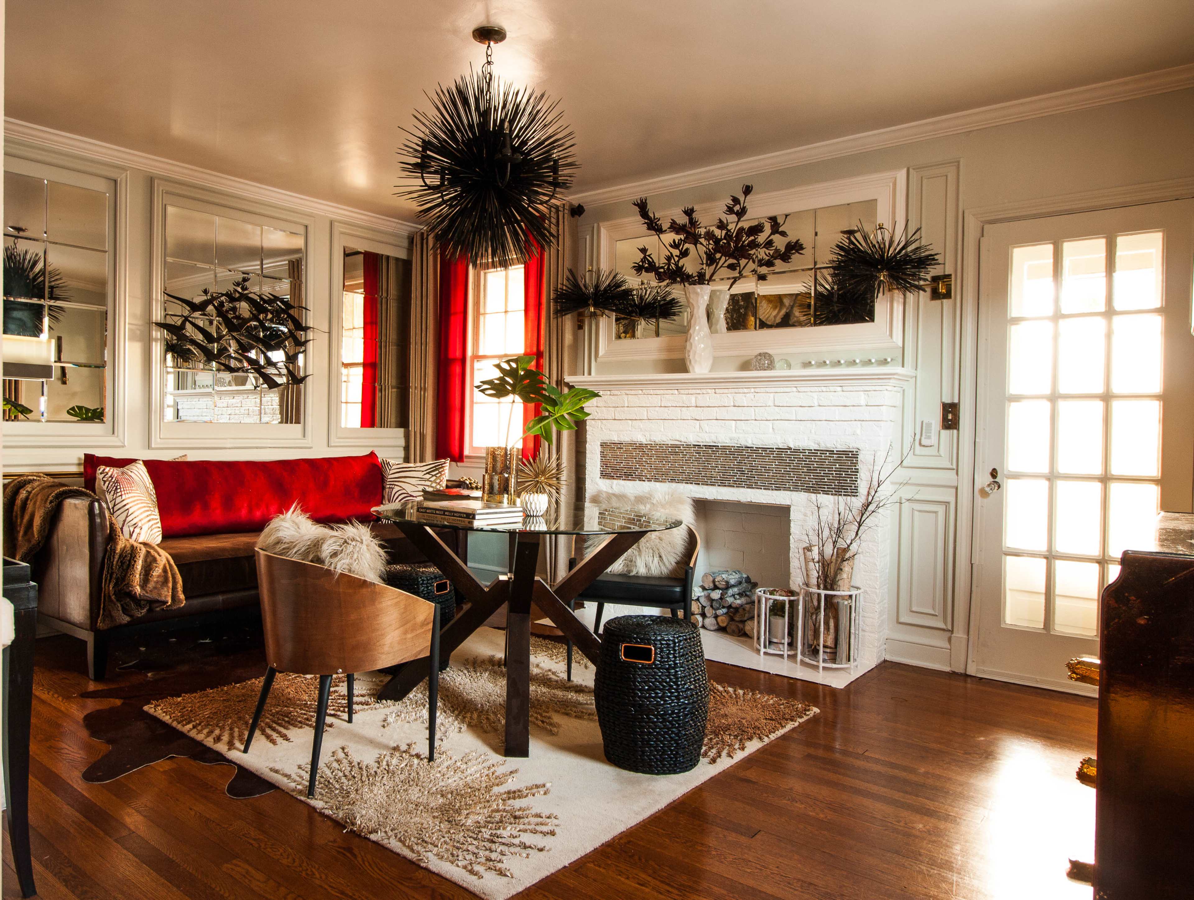 A stylish living room featuring a dark wooden floor, a round glass dining table, upholstered seating with red accents, and a modern light fixture above.