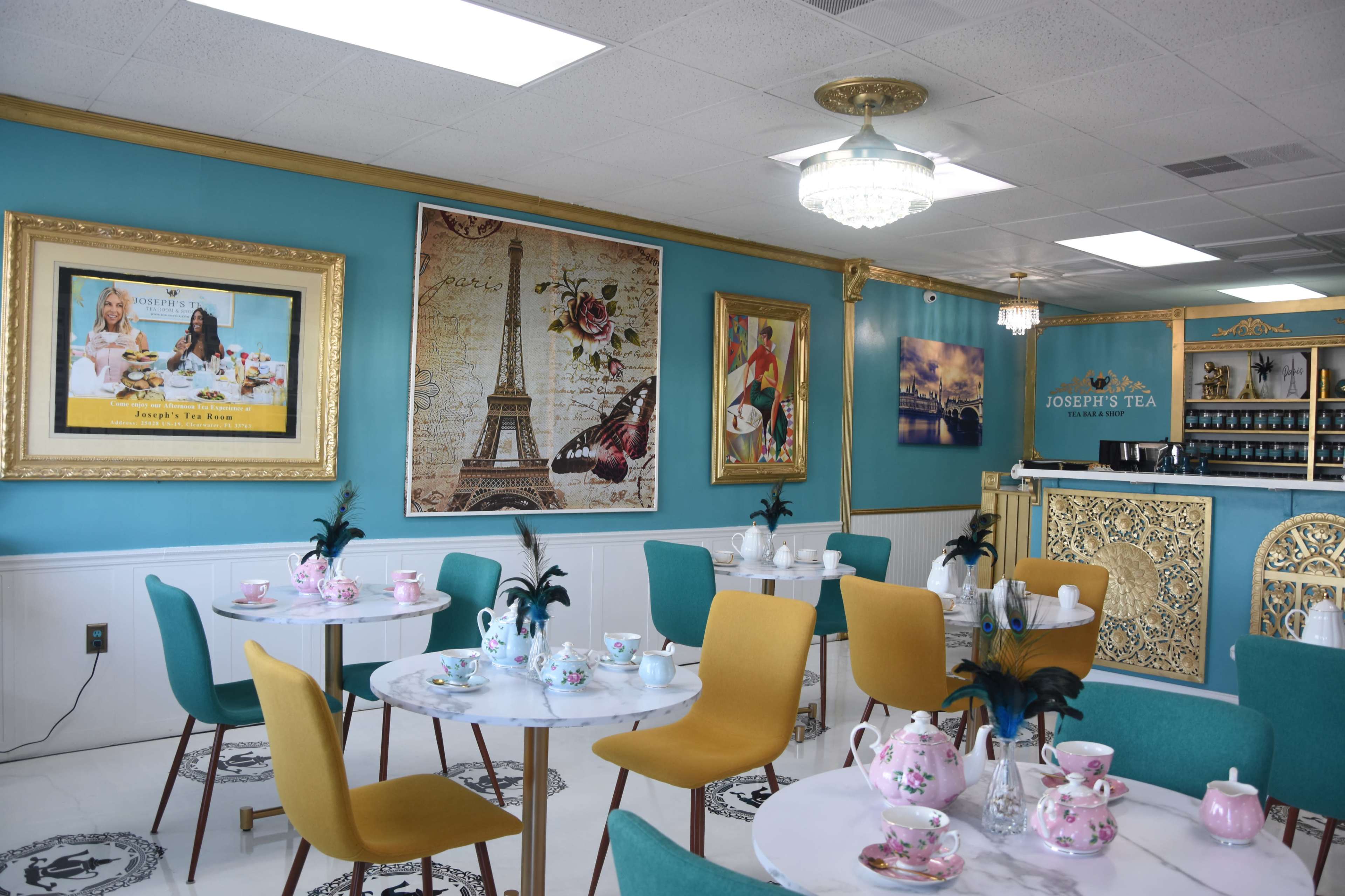 A tea room with turquoise walls, elegant decor, and tables set with tea cups and pastries.