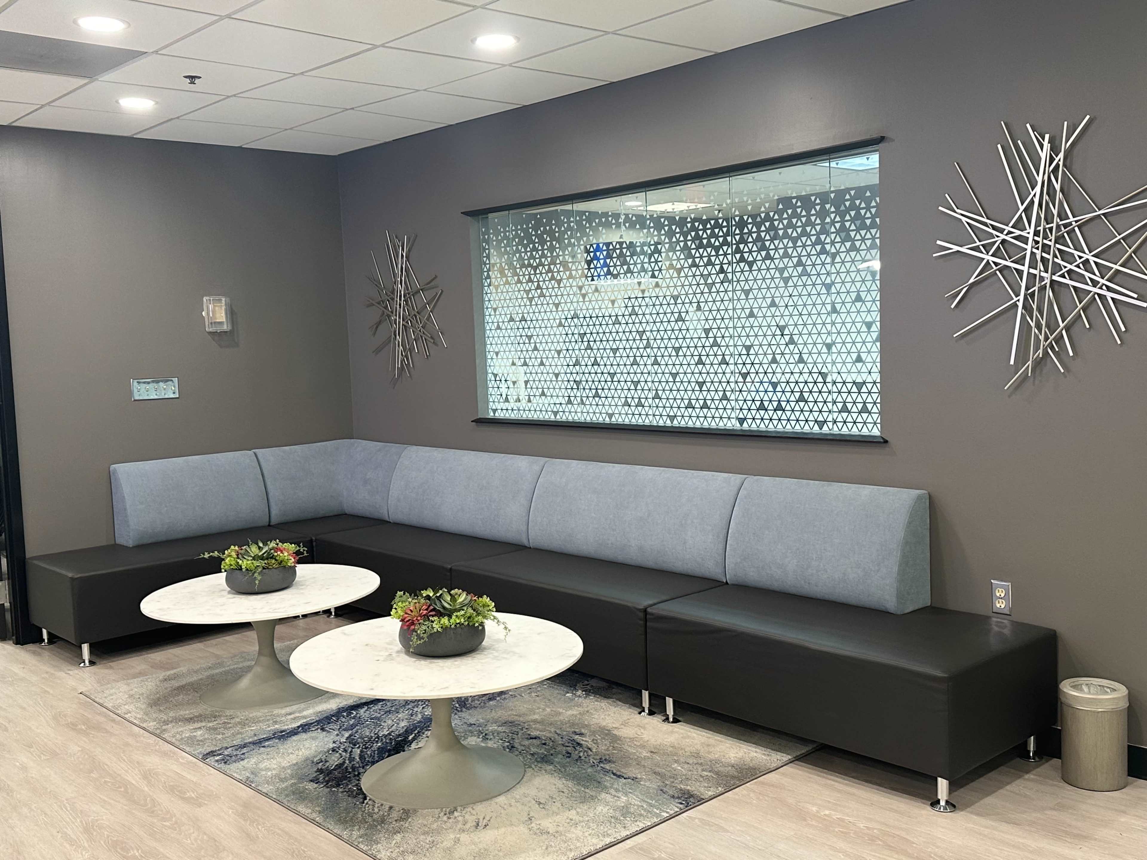 A modern waiting area featuring a gray upholstered bench and two circular tables with decorative plants.