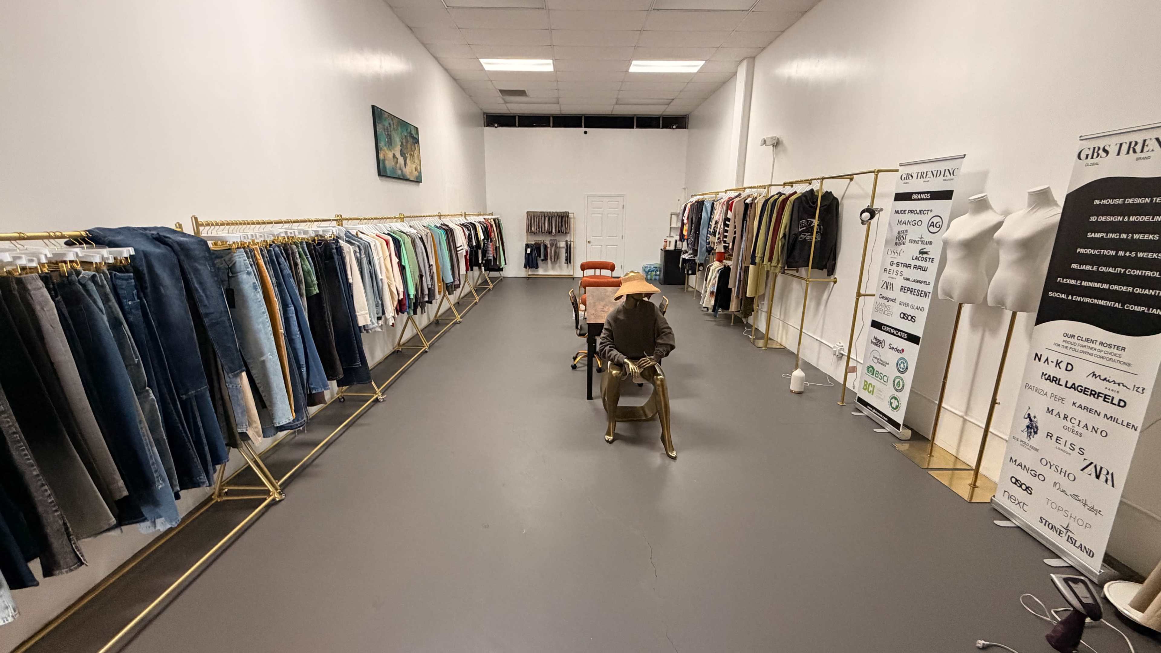 The image shows a clothing store interior with rows of garments on gold racks, a central display mannequin, and promotional banners along the walls.