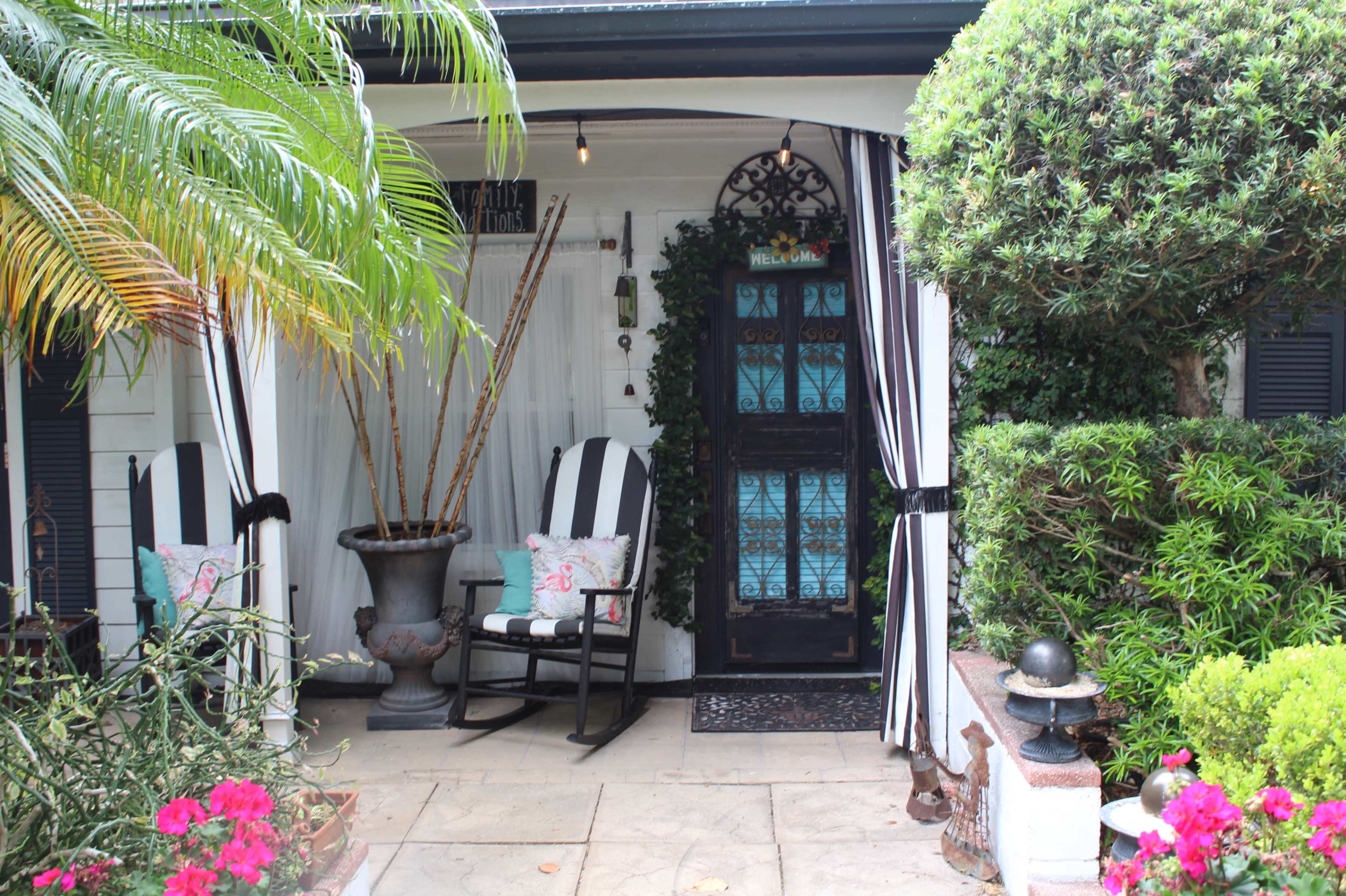 The image shows a cozy porch area with striped rocking chairs, potted plants, and a decorative door adorned with intricate glass.