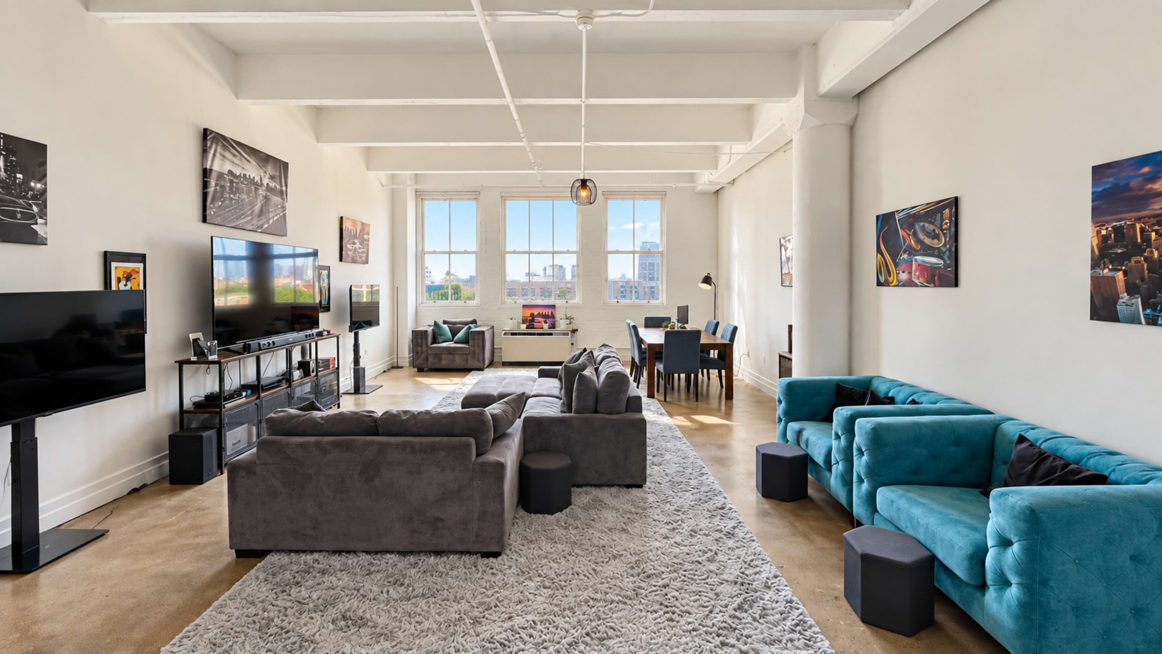 The image depicts a spacious living area with a mix of gray and teal couches, a large television, and a dining table near a wall of windows.