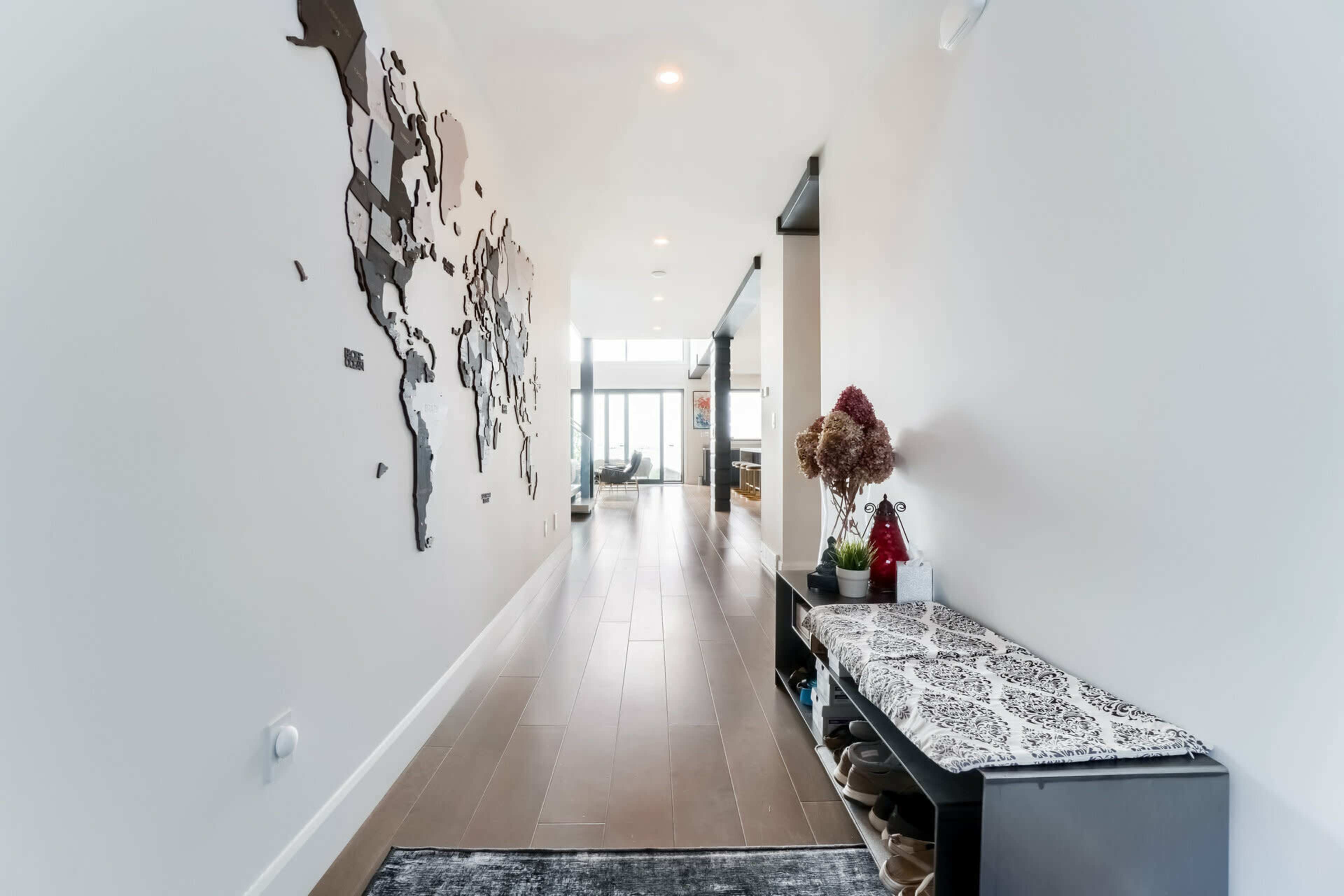 A hallway features a world map on the wall and a bench with shoes and decorative items beside it.