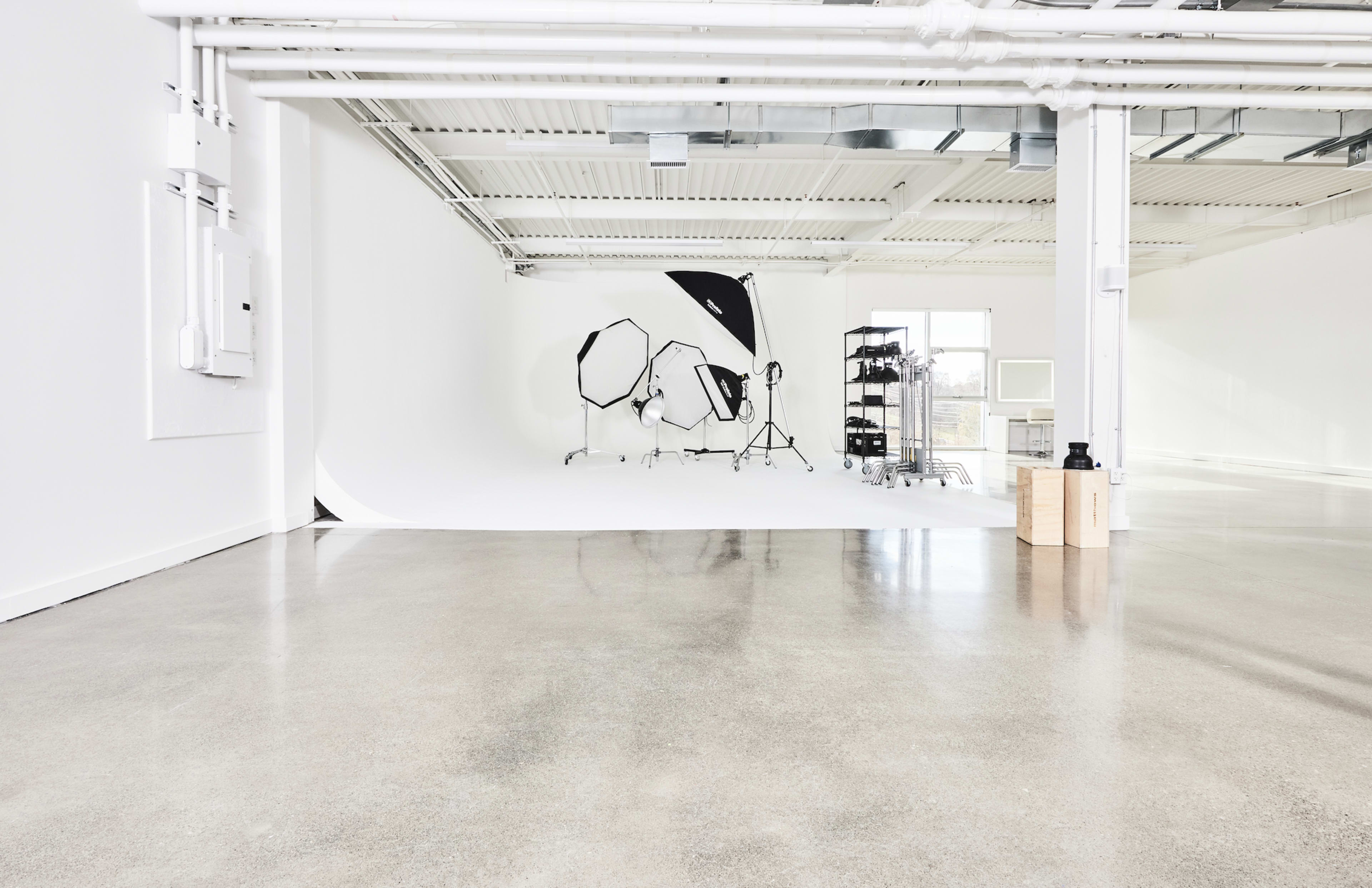 A spacious photography studio with a white backdrop, lighting equipment, and polished concrete floors.