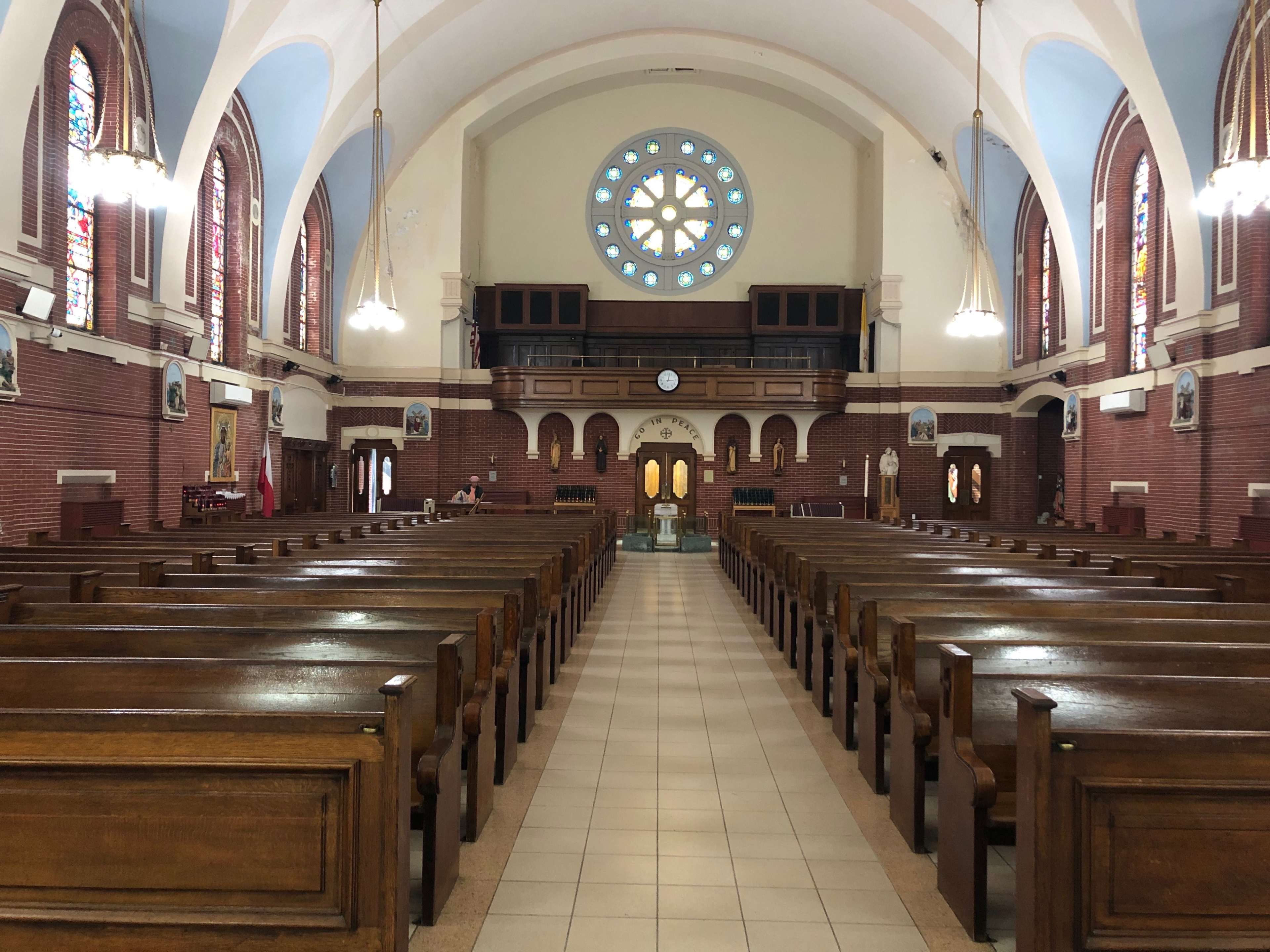 The interior of a large church with wooden pews arranged in rows and a circular stained glass window at the far end.