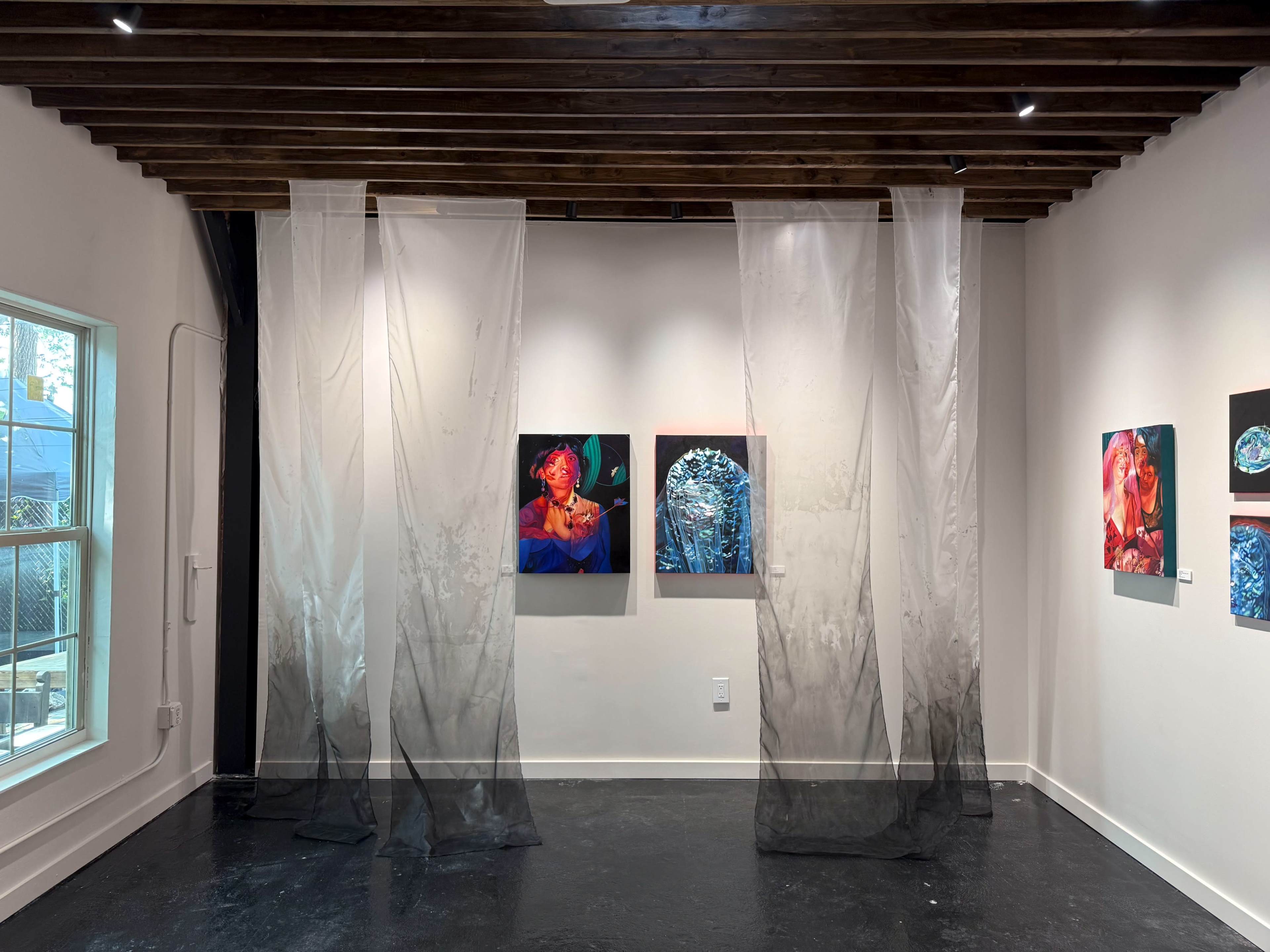 The image shows an art gallery featuring two paintings on the walls, with sheer fabric draping from the ceiling creating a partition in the space.