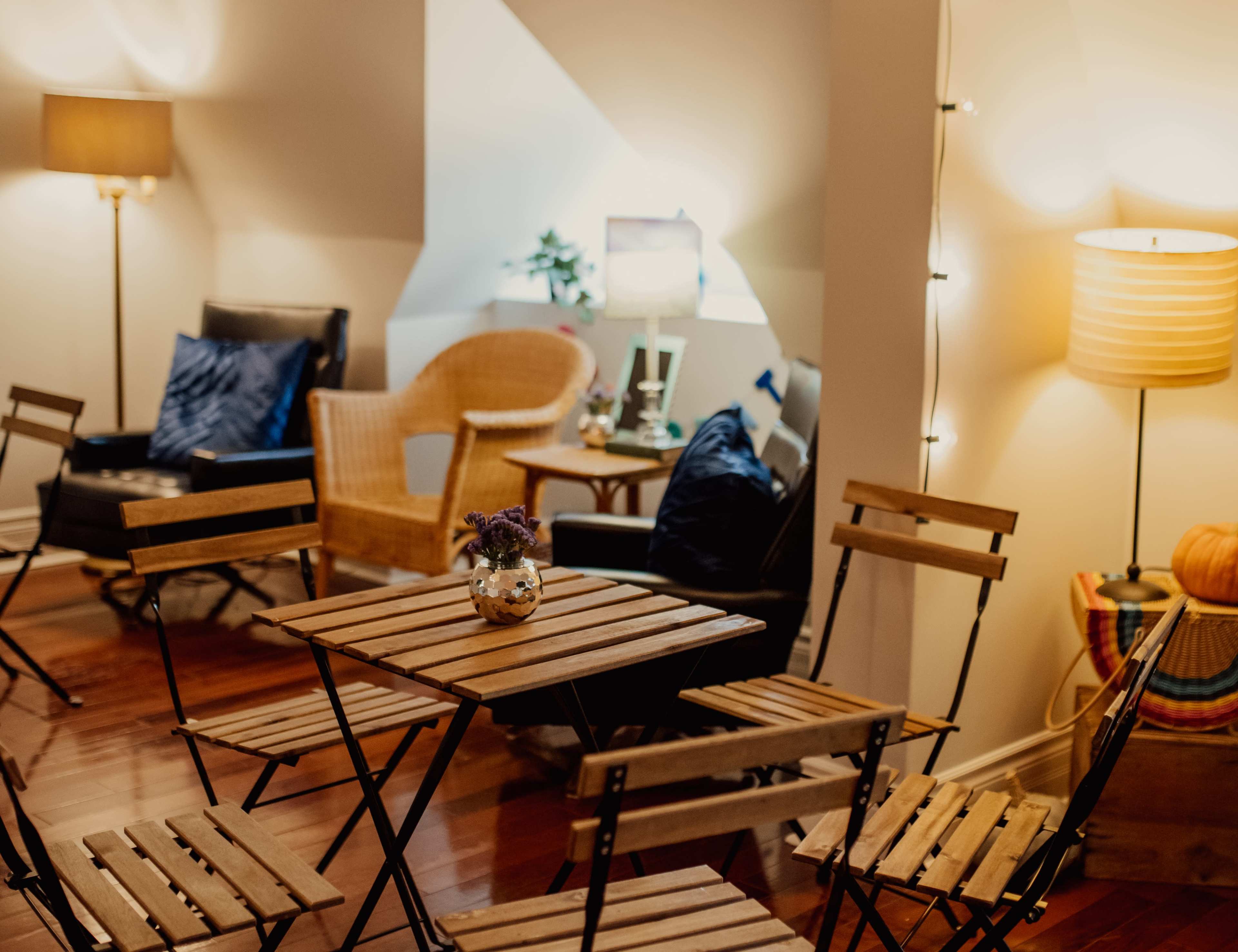 The scene features a cozy room with wooden folding chairs and a small table at the center, surrounded by soft lighting and seating areas.