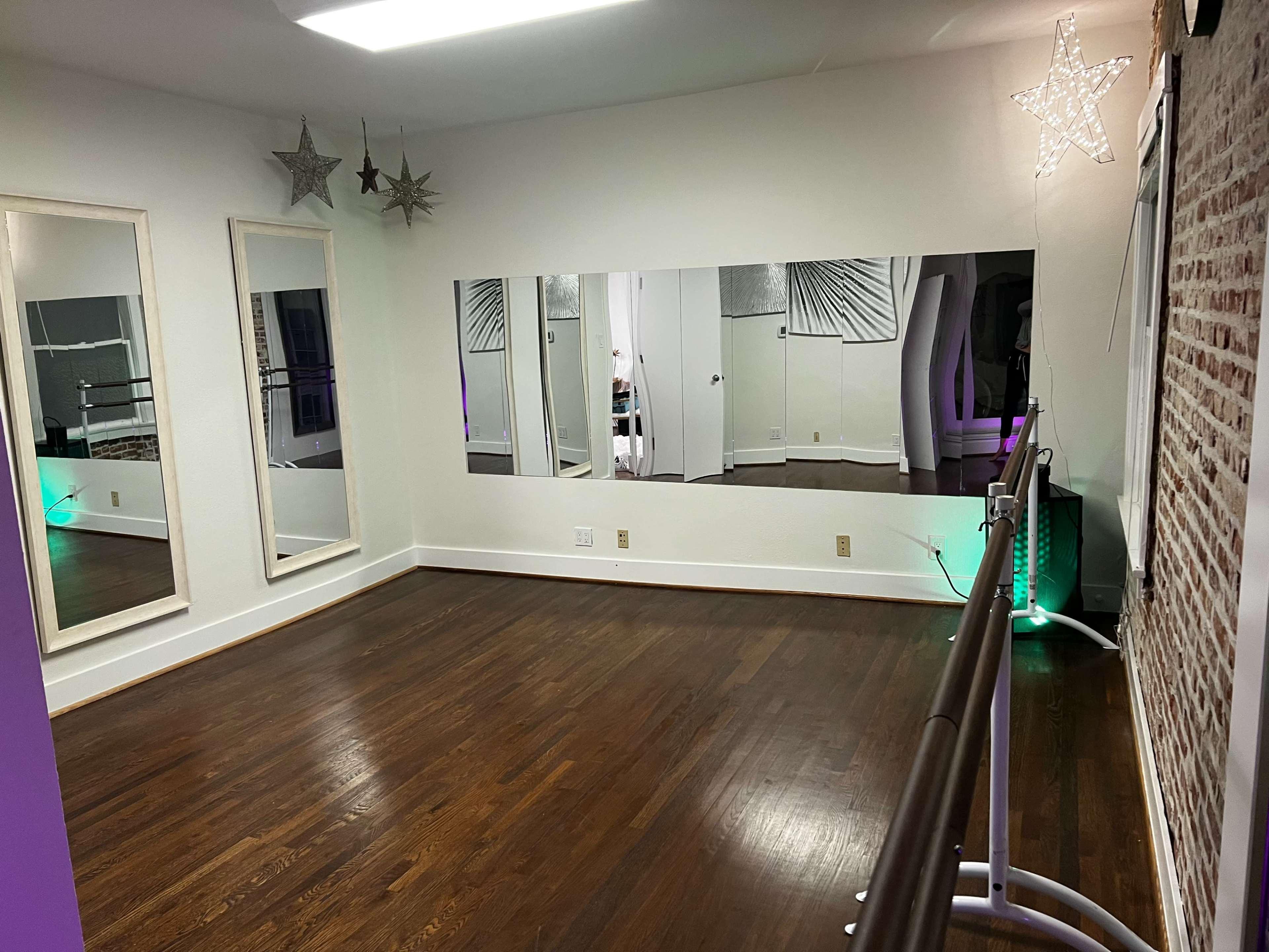 A spacious dance studio features wooden floors, mirrored walls, and a ballet barre illuminated by green light.