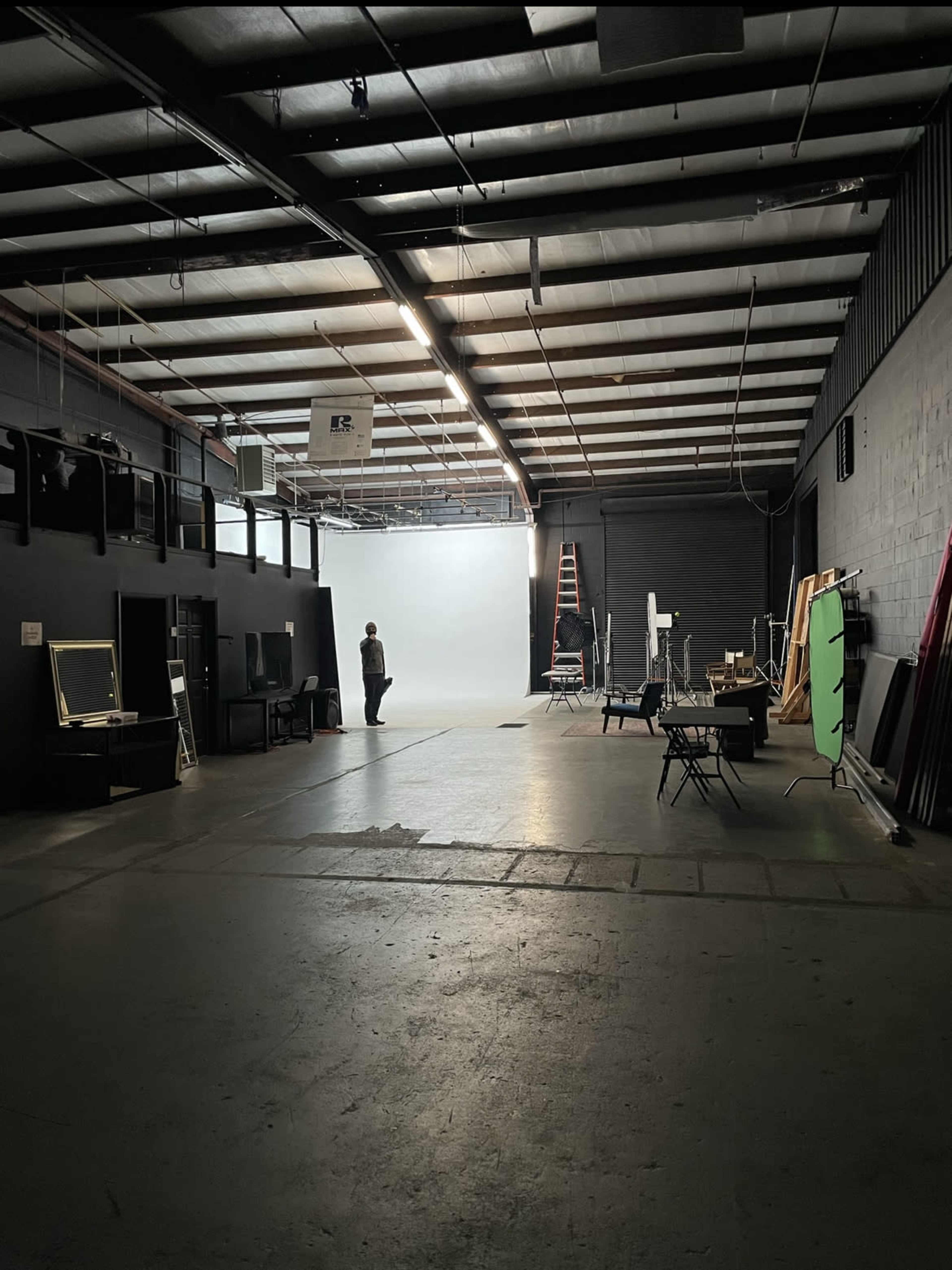 A person stands in a spacious studio with a light gray backdrop, surrounded by various equipment and props.