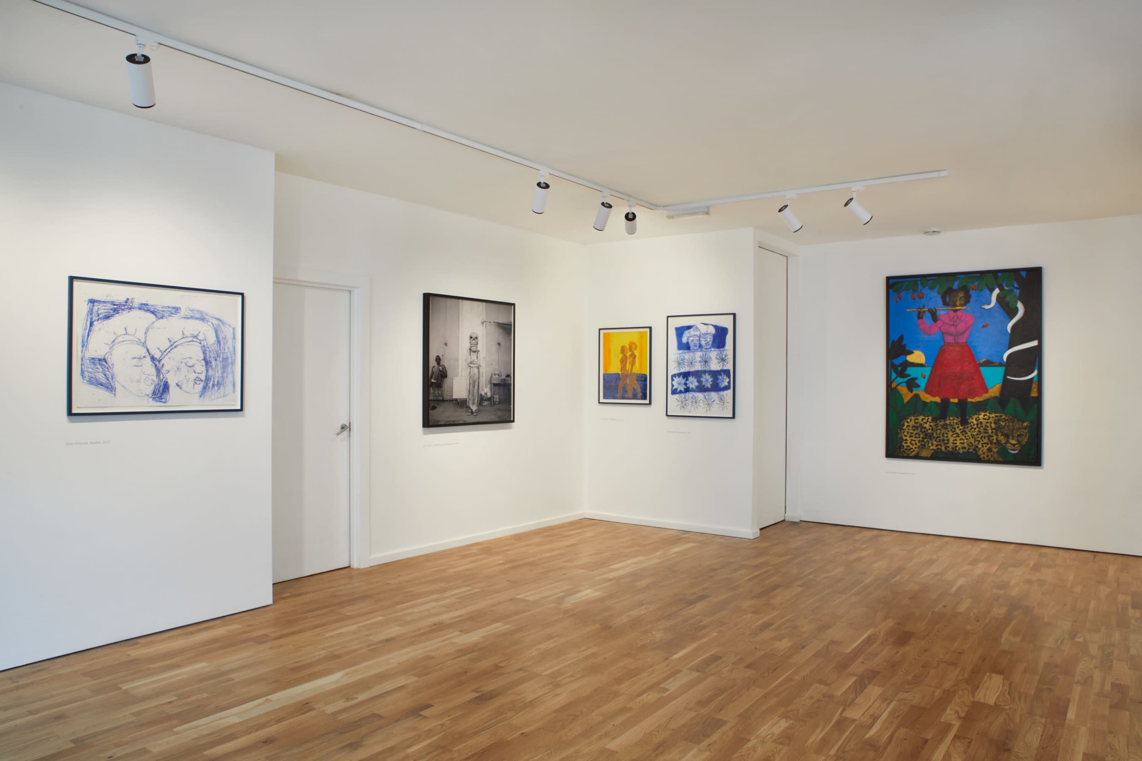 An art gallery with wooden flooring displaying various framed artworks on white walls.