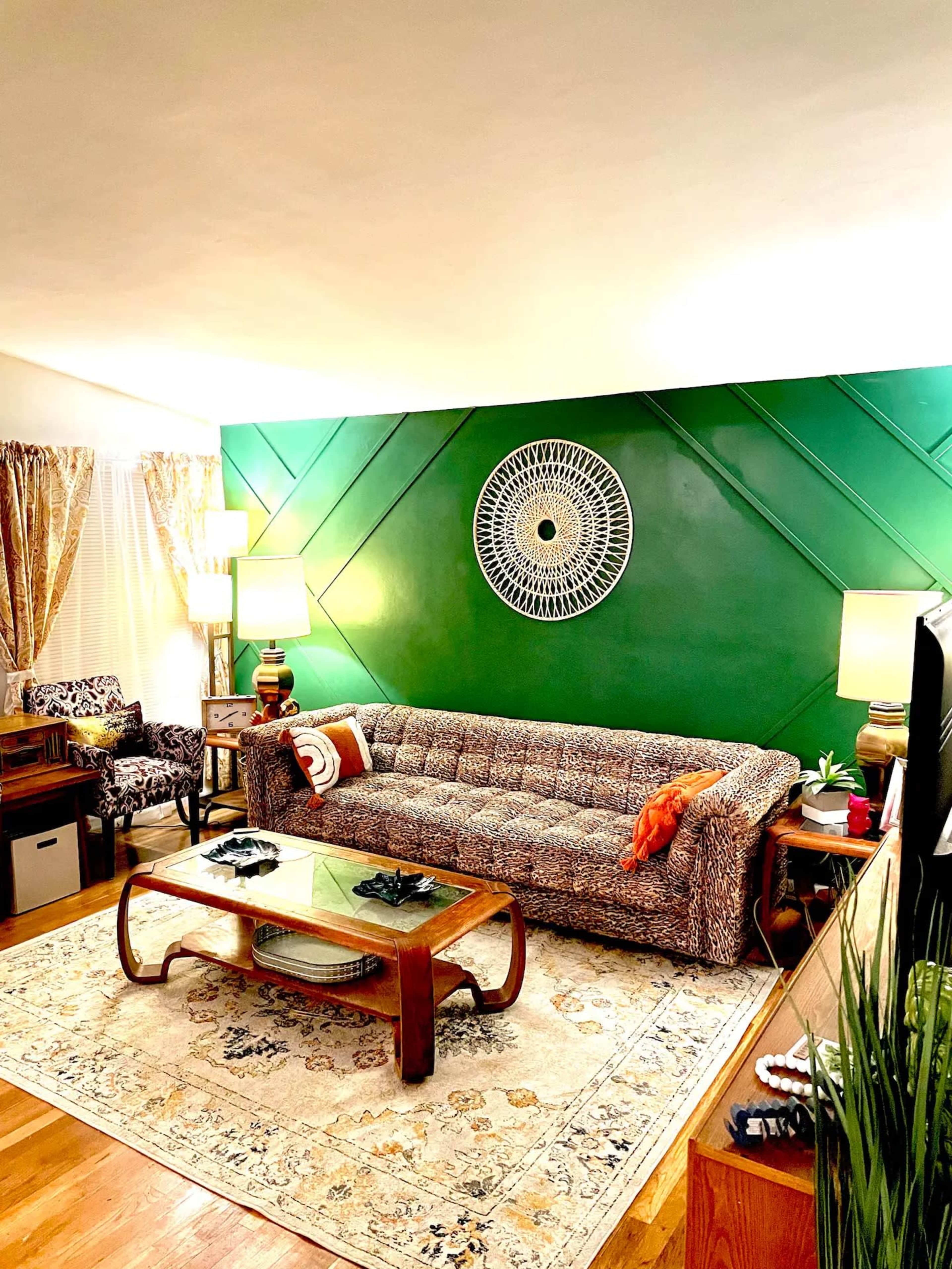The living room features a patterned sofa, a glass coffee table, and a bold green accent wall with a circular wall decoration.