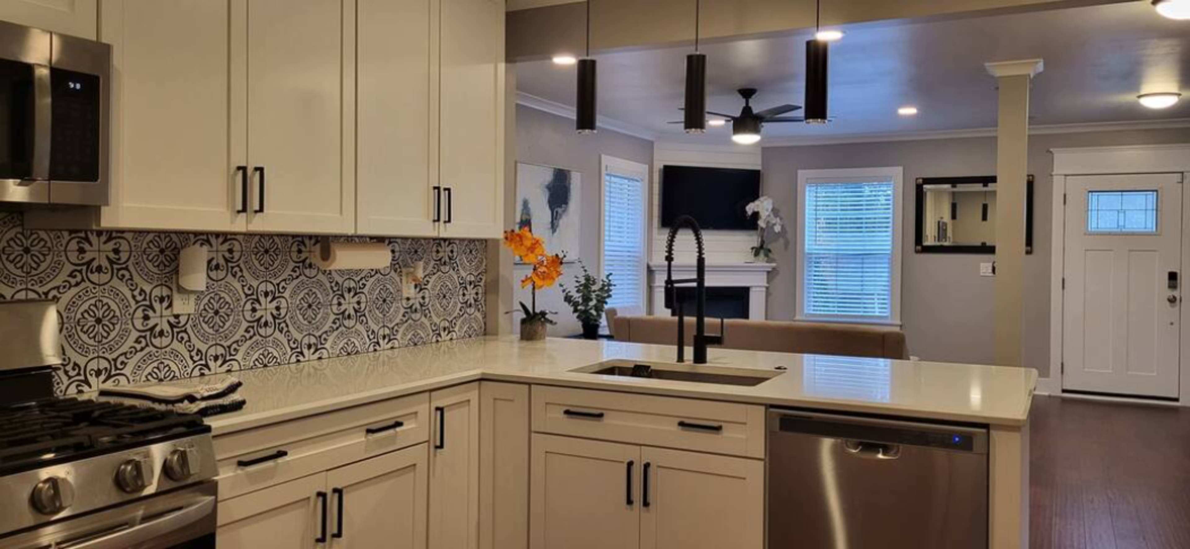 A modern kitchen with white cabinetry, a patterned backsplash, and stainless steel appliances, transitioning to a living area with a sofa and television.