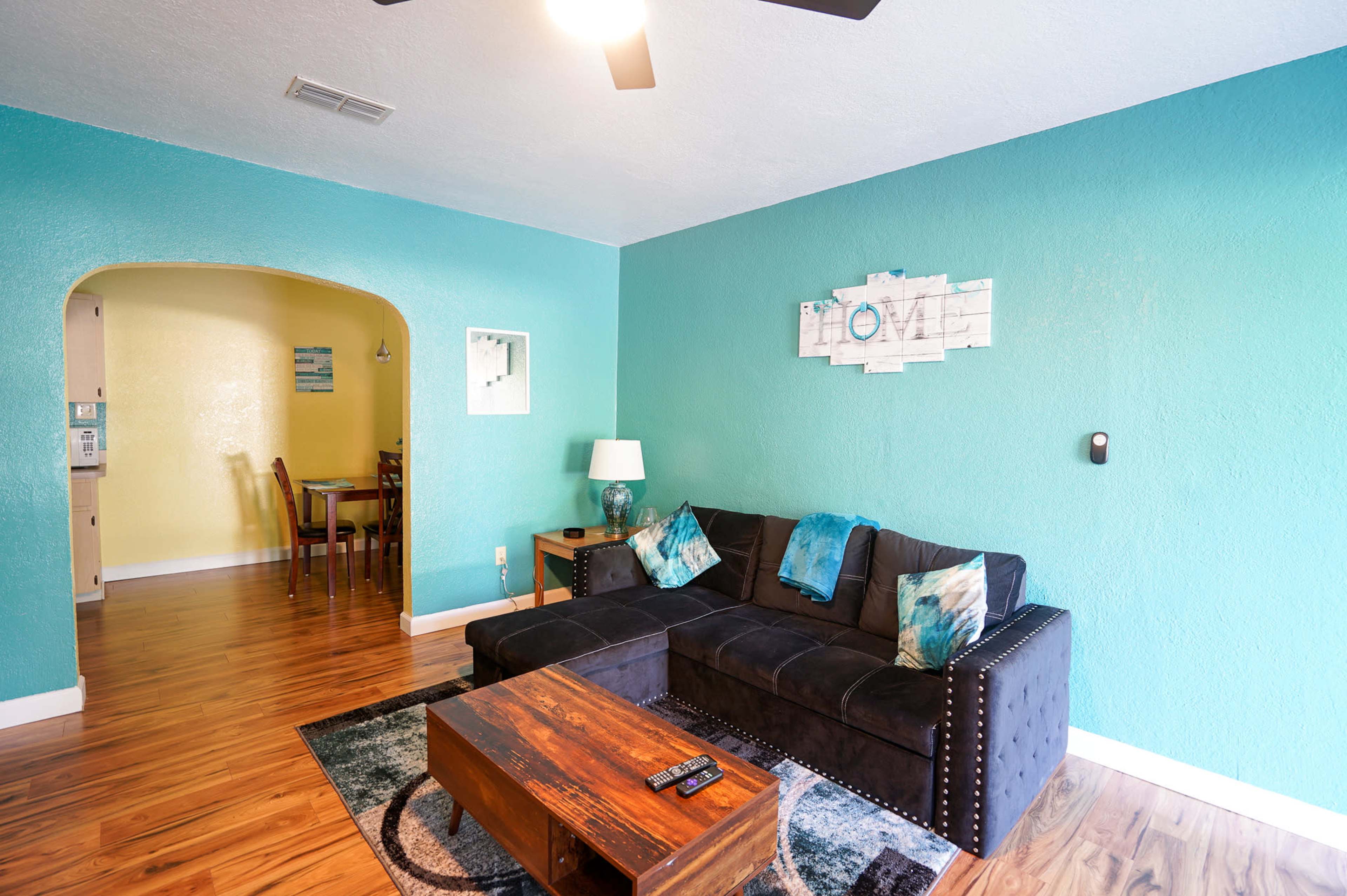 The living room features a dark sectional sofa and a wooden coffee table, with turquoise walls and hardwood flooring.