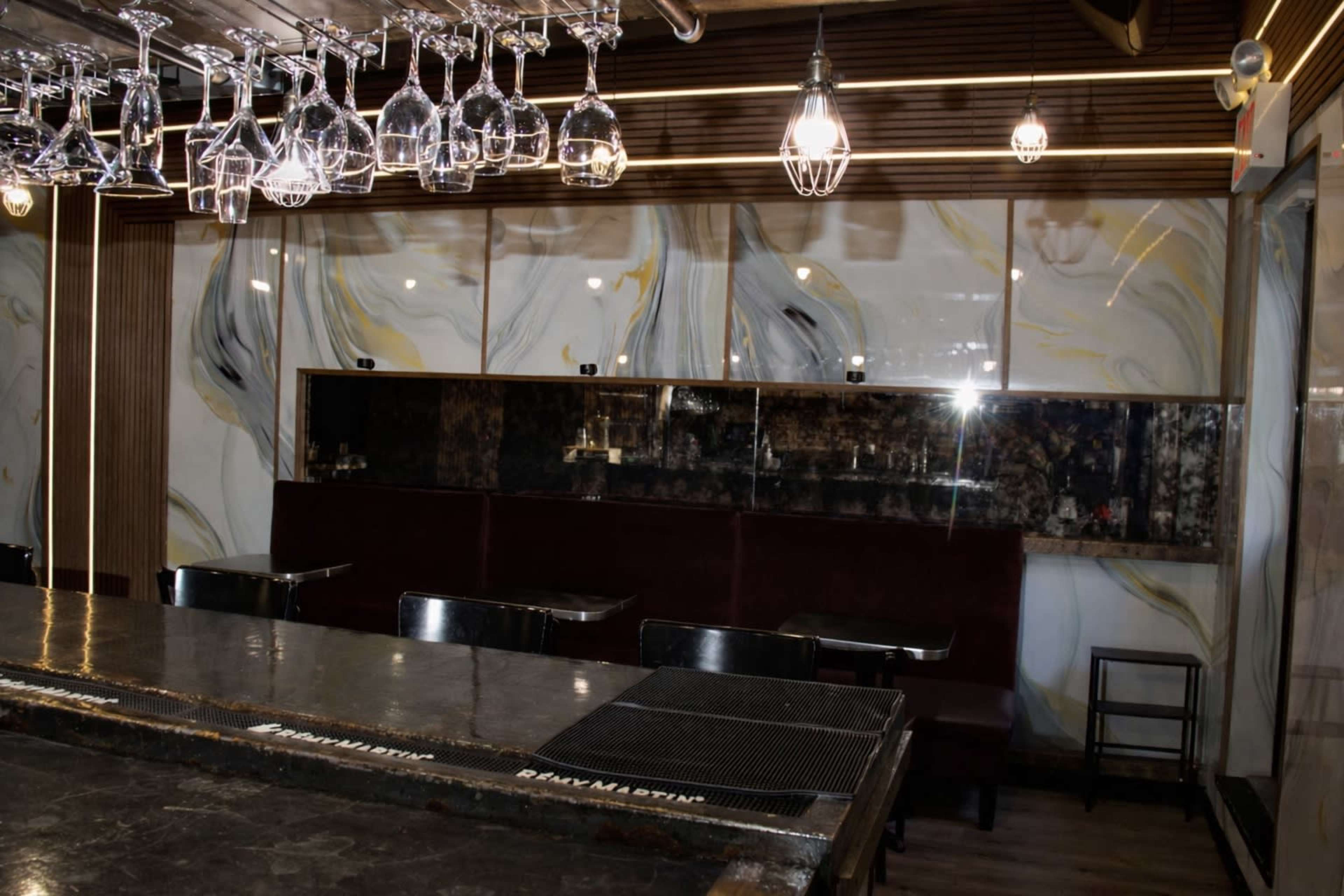 The image shows an empty bar area with a dark countertop, wine glasses hanging above, and marble-patterned walls.