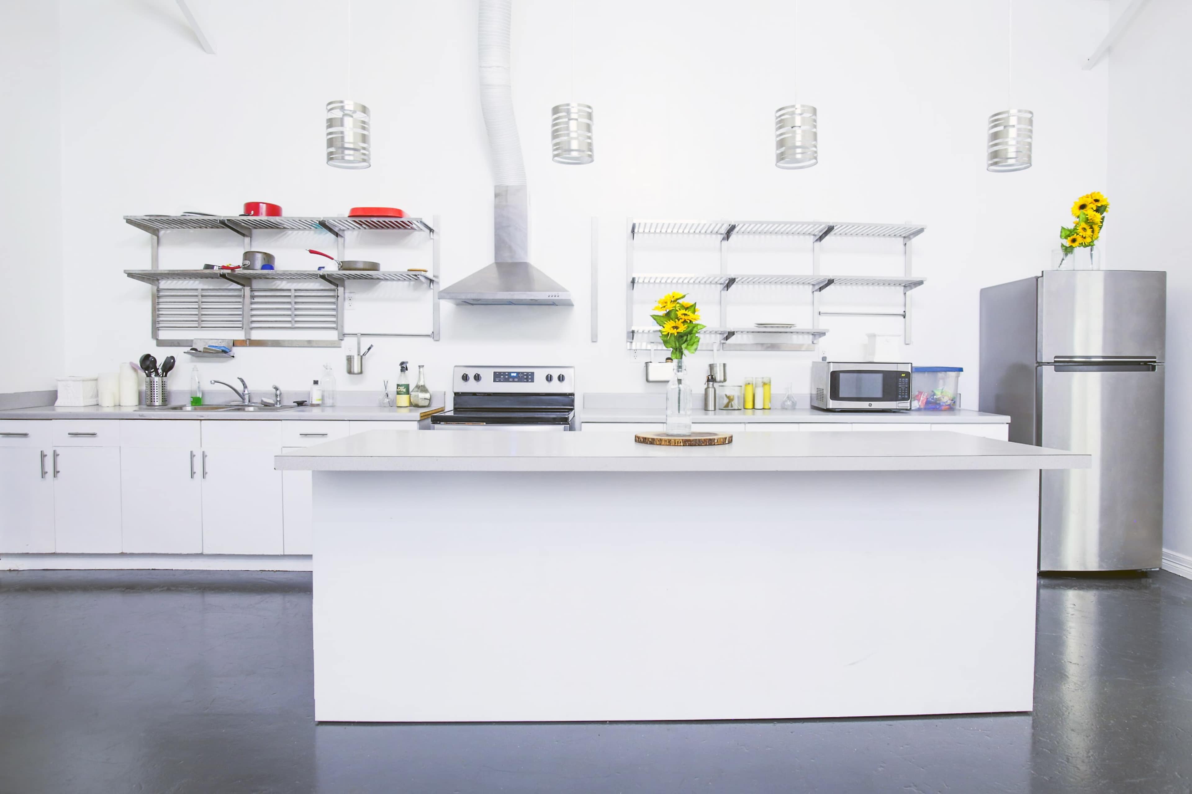 A modern kitchen with white cabinetry, stainless steel appliances, and open shelving adorned with yellow flowers.