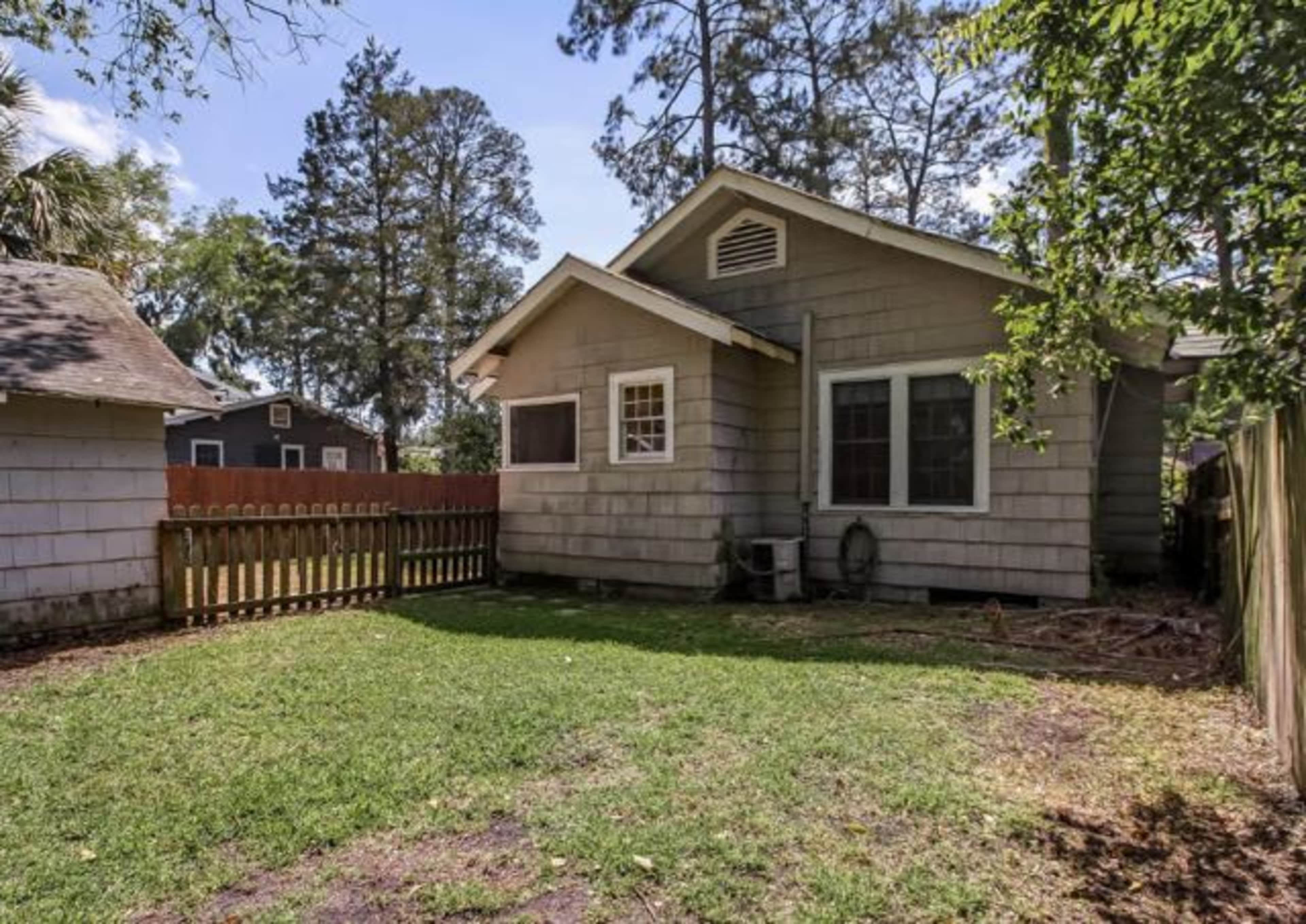 The backyard of a house with a grassy area, wooden fence, and trees in the background.