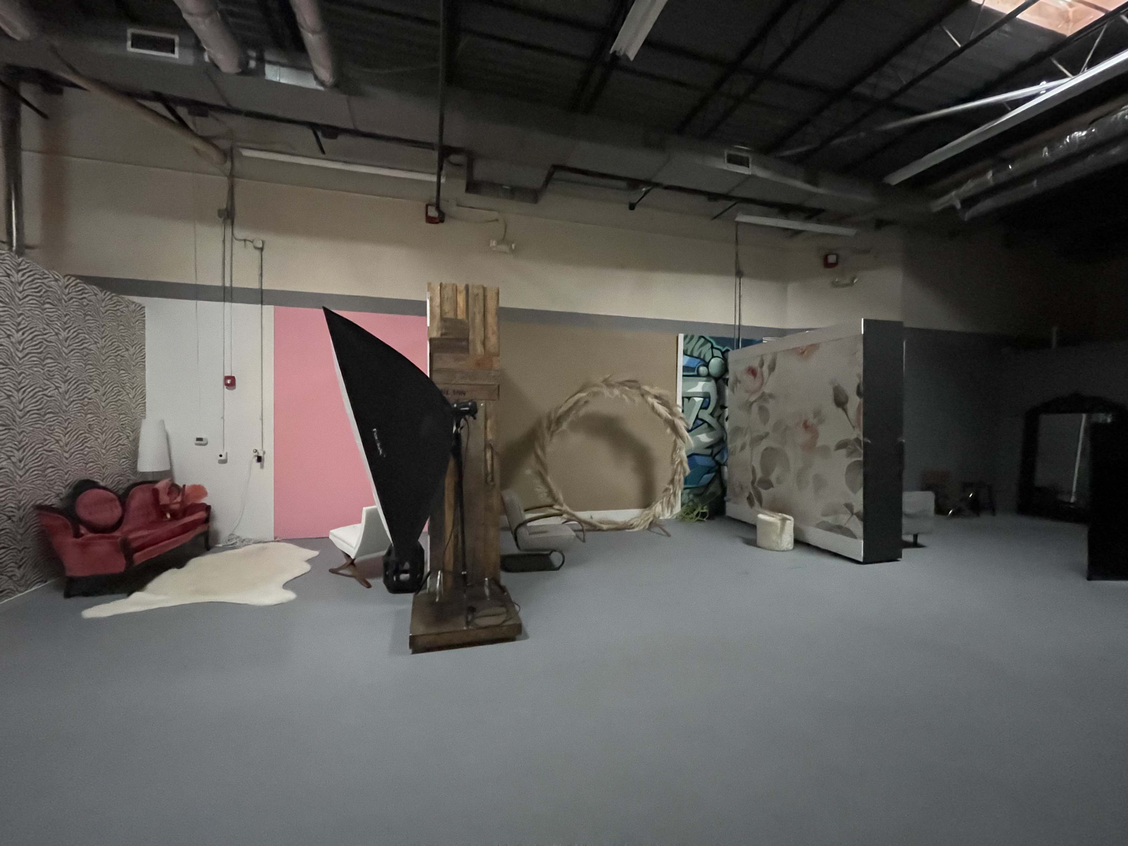 An empty studio space with various backdrops and props, including a red couch and an easel.