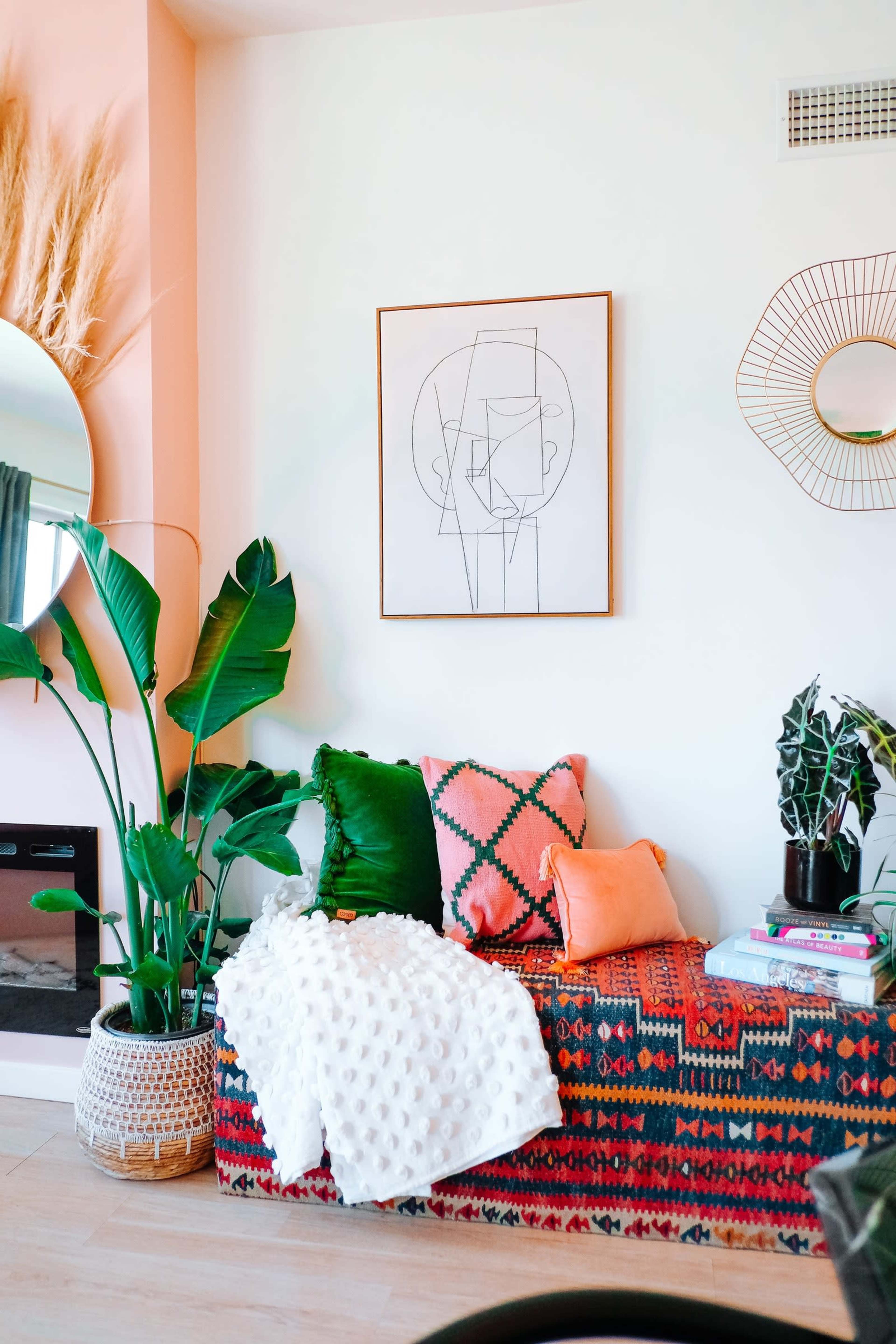 A colorful seating area features a patterned bench adorned with pillows and a throw, accompanied by decorative plants and framed artwork on the wall.