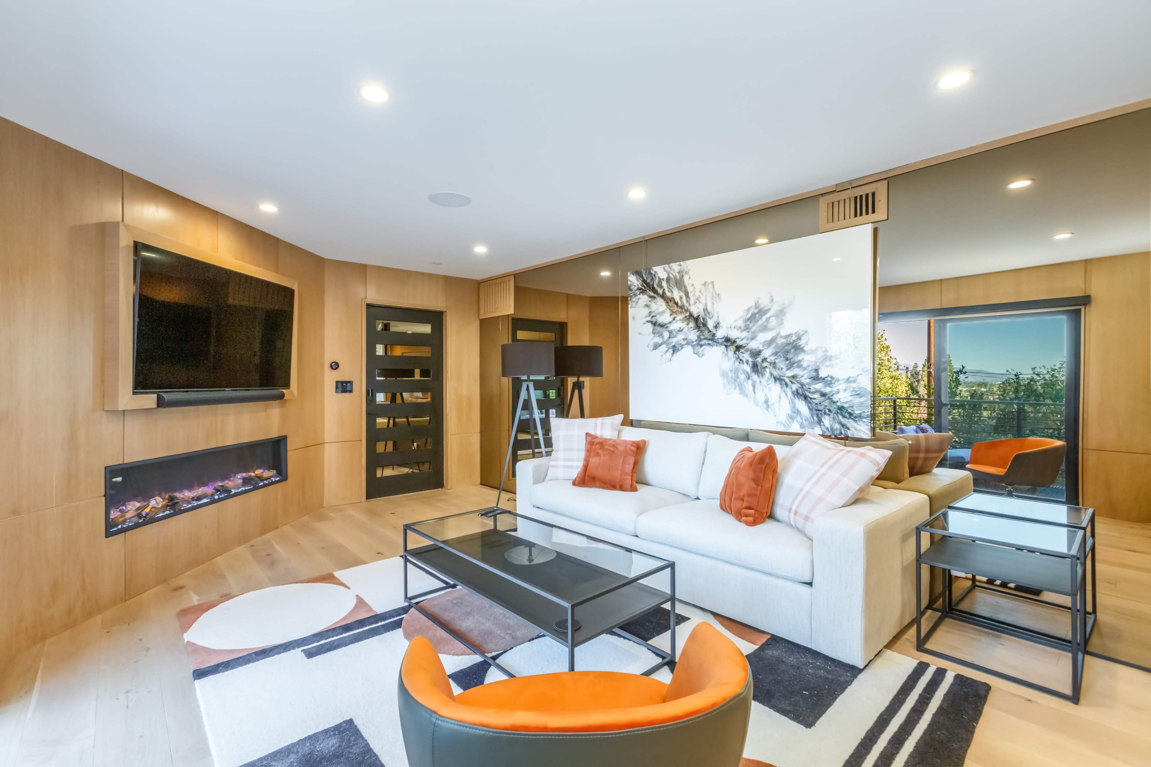 A modern living room with a light-colored sofa, a television on the wall, a coffee table, and large windows that provide natural light.