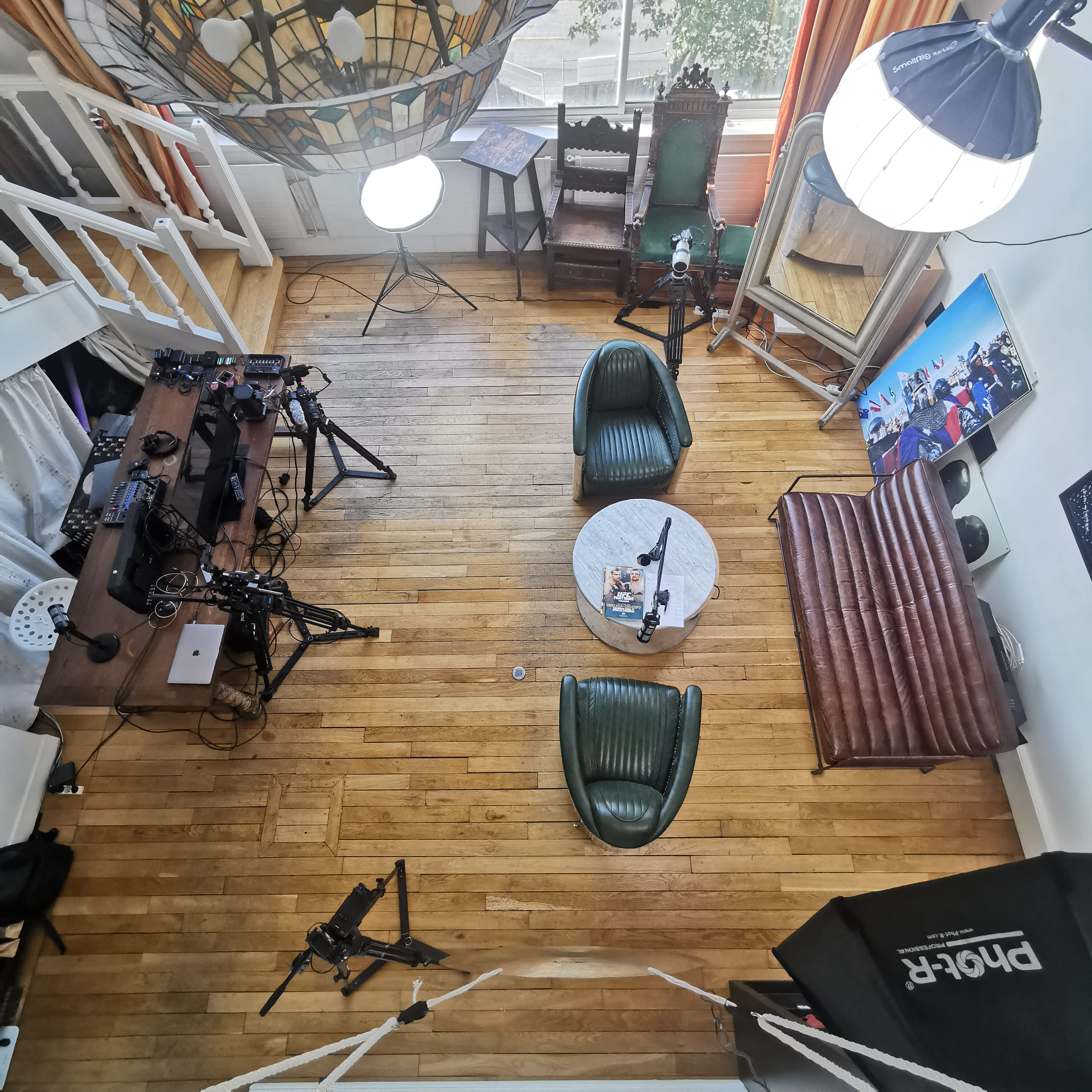 A well-arranged studio space featuring two green chairs, a coffee table, and various cameras and lighting equipment set up on a wooden floor.