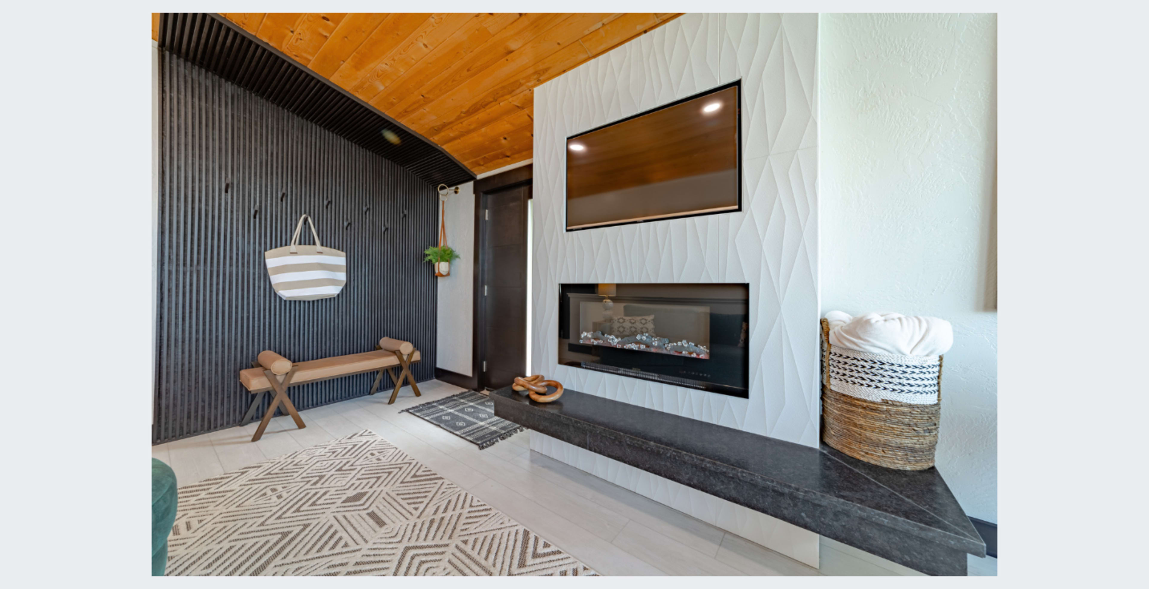 The image shows a modern living room with a wall-mounted television above a fireplace, a patterned rug on the floor, and a bench along one side.