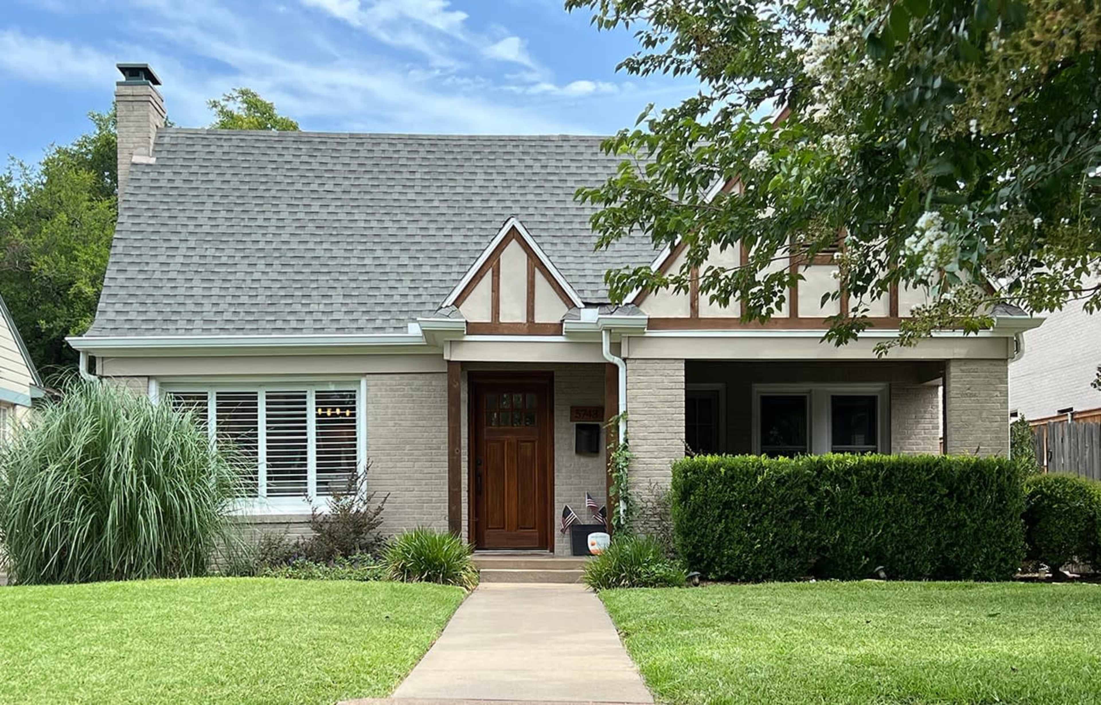 A two-story house with a steeply pitched roof features a brick facade and decorative timber accents.