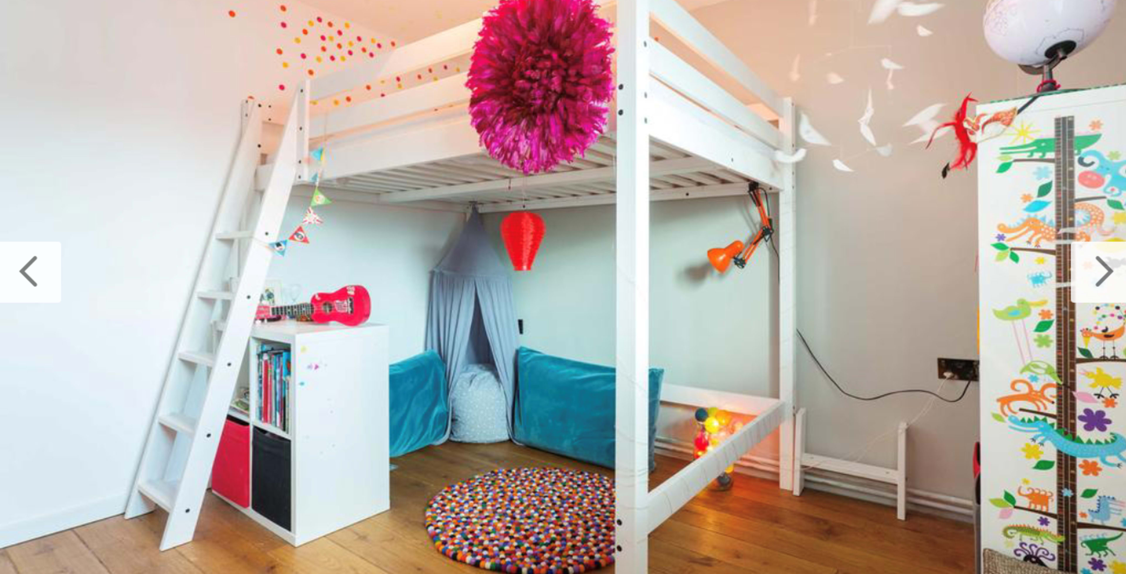 A modern children's bedroom featuring a loft bed, two lower beds, colorful decorations, and a round rug on a wooden floor.