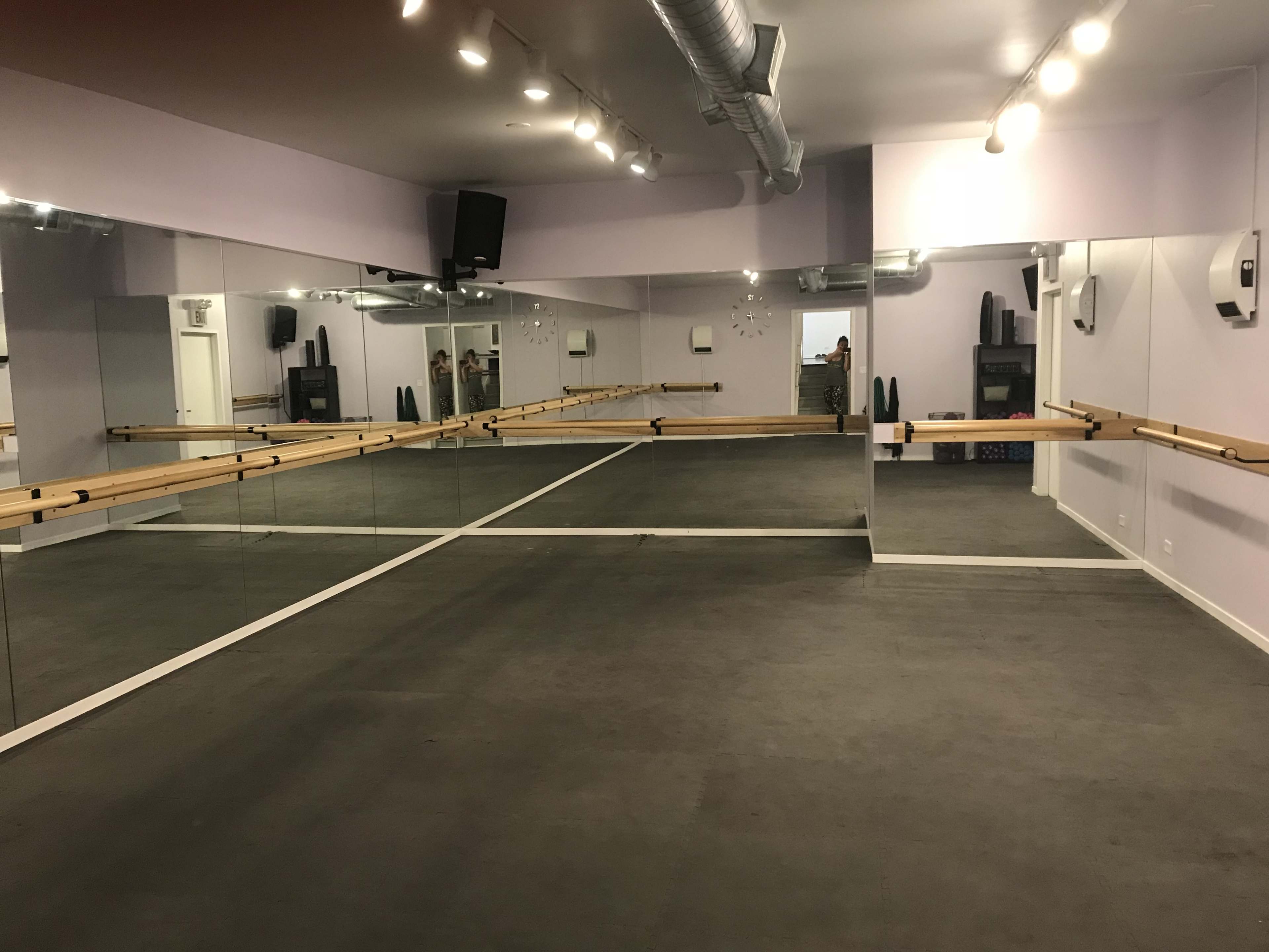 A mirrored dance studio with wooden barre along the walls and a gray floor.