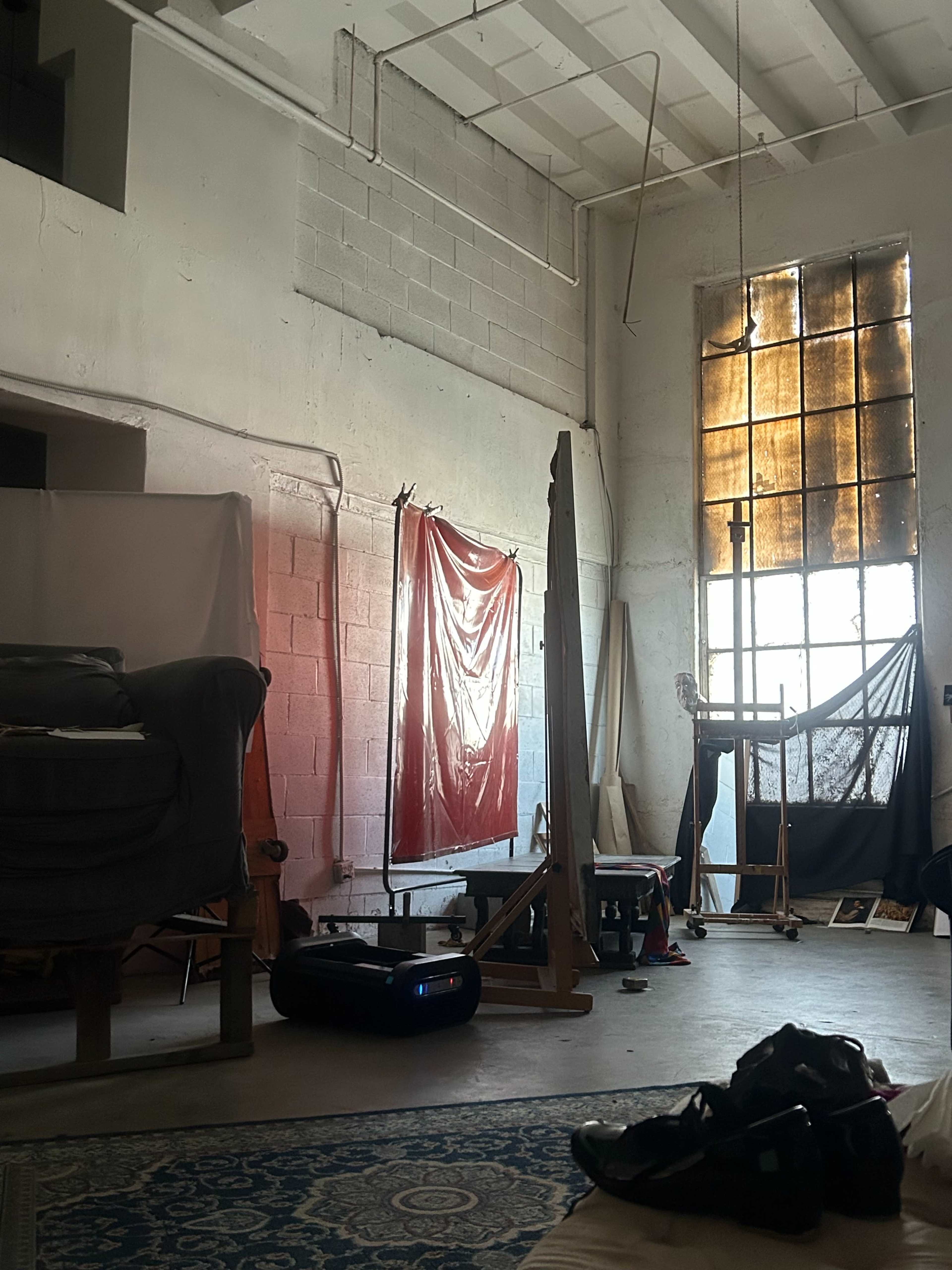 The image shows an art studio with various equipment, including a red curtain, easel, and cluttered floor.