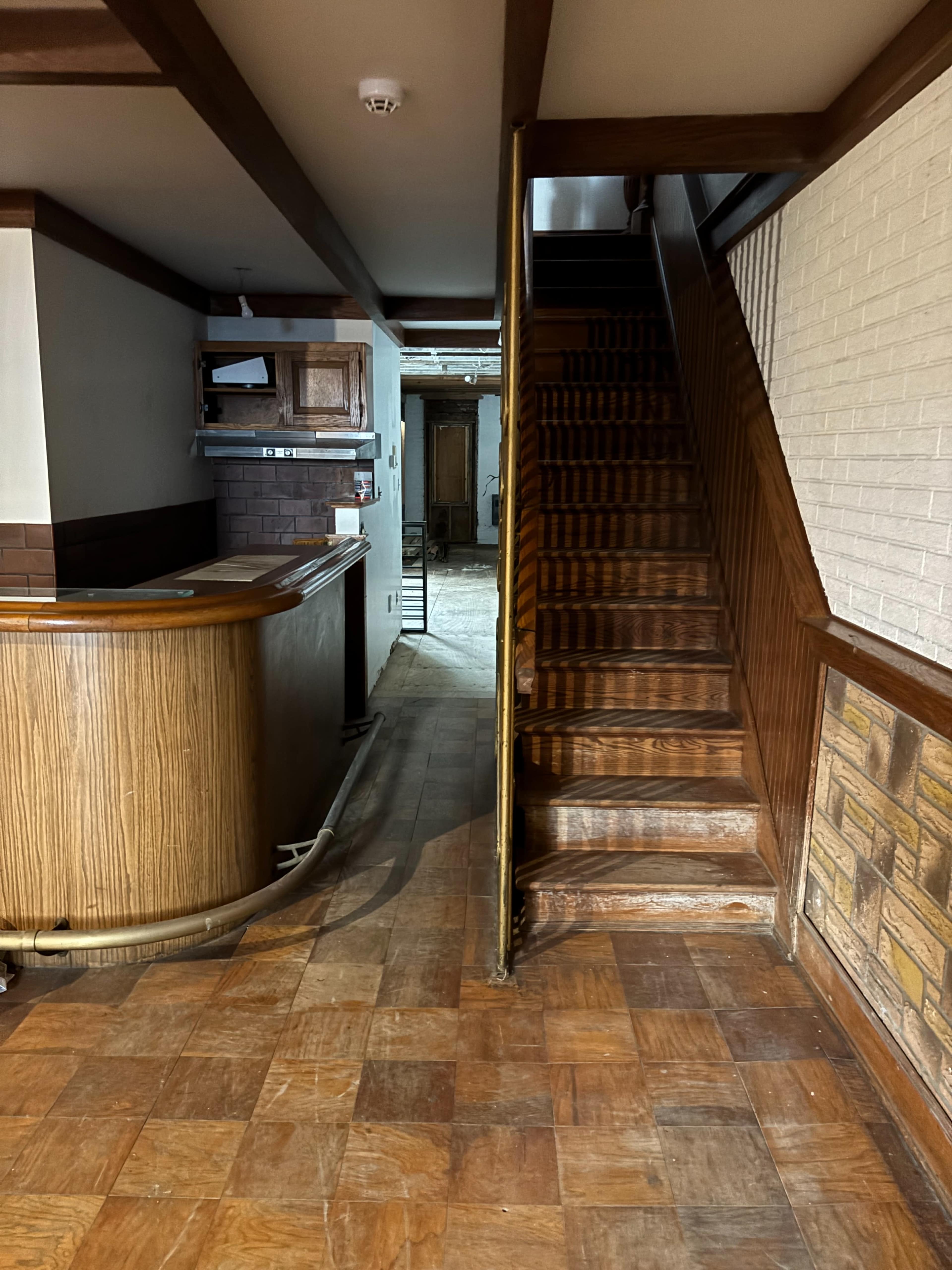 The image shows a hallway with wooden flooring, a bar counter on the left, and a staircase leading to an upper level on the right.