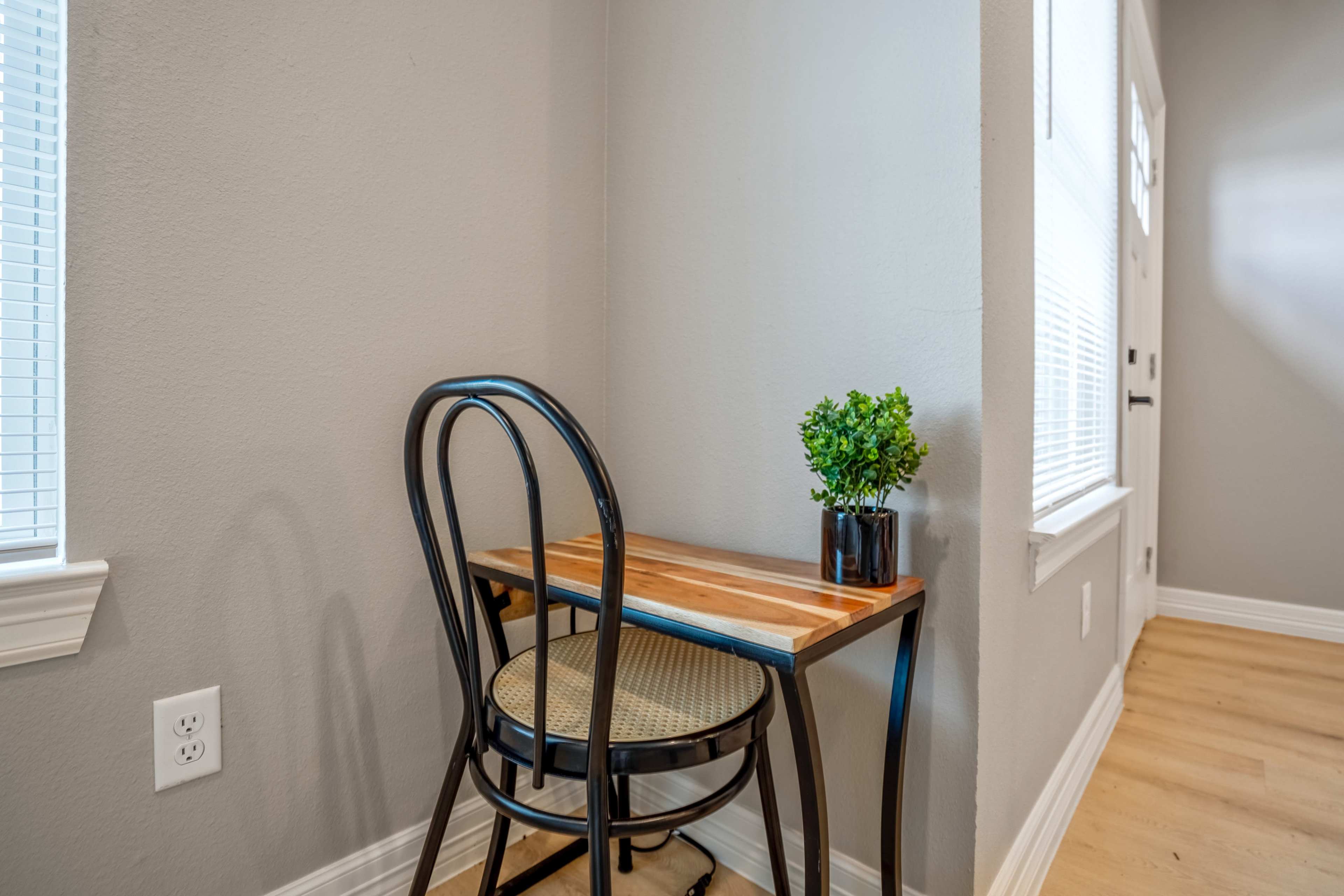 A small wooden table with a black chair and a potted plant sits in a corner near a window.