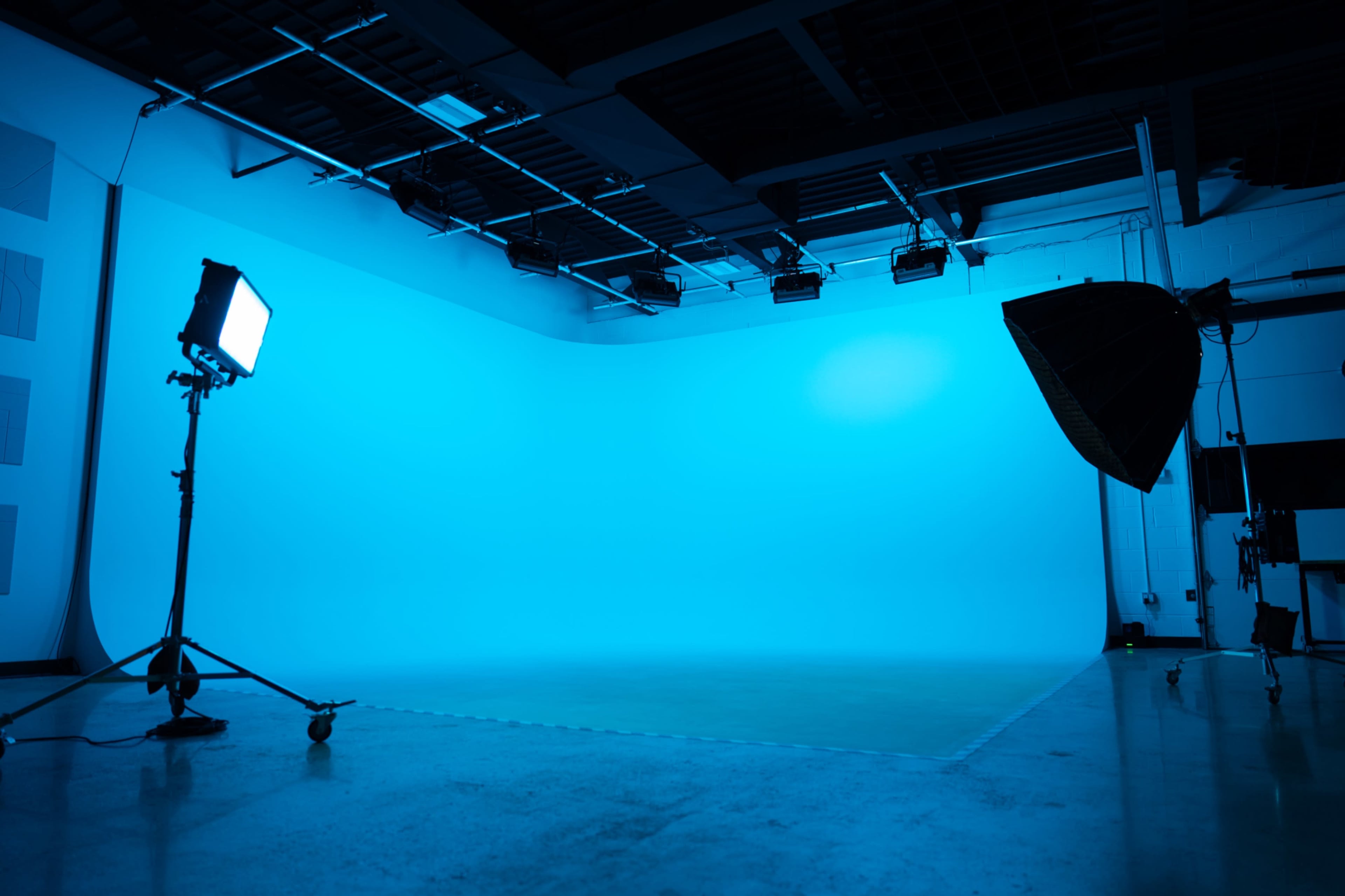 The image shows a photography studio with a seamless blue backdrop and various lighting equipment positioned on the floor.