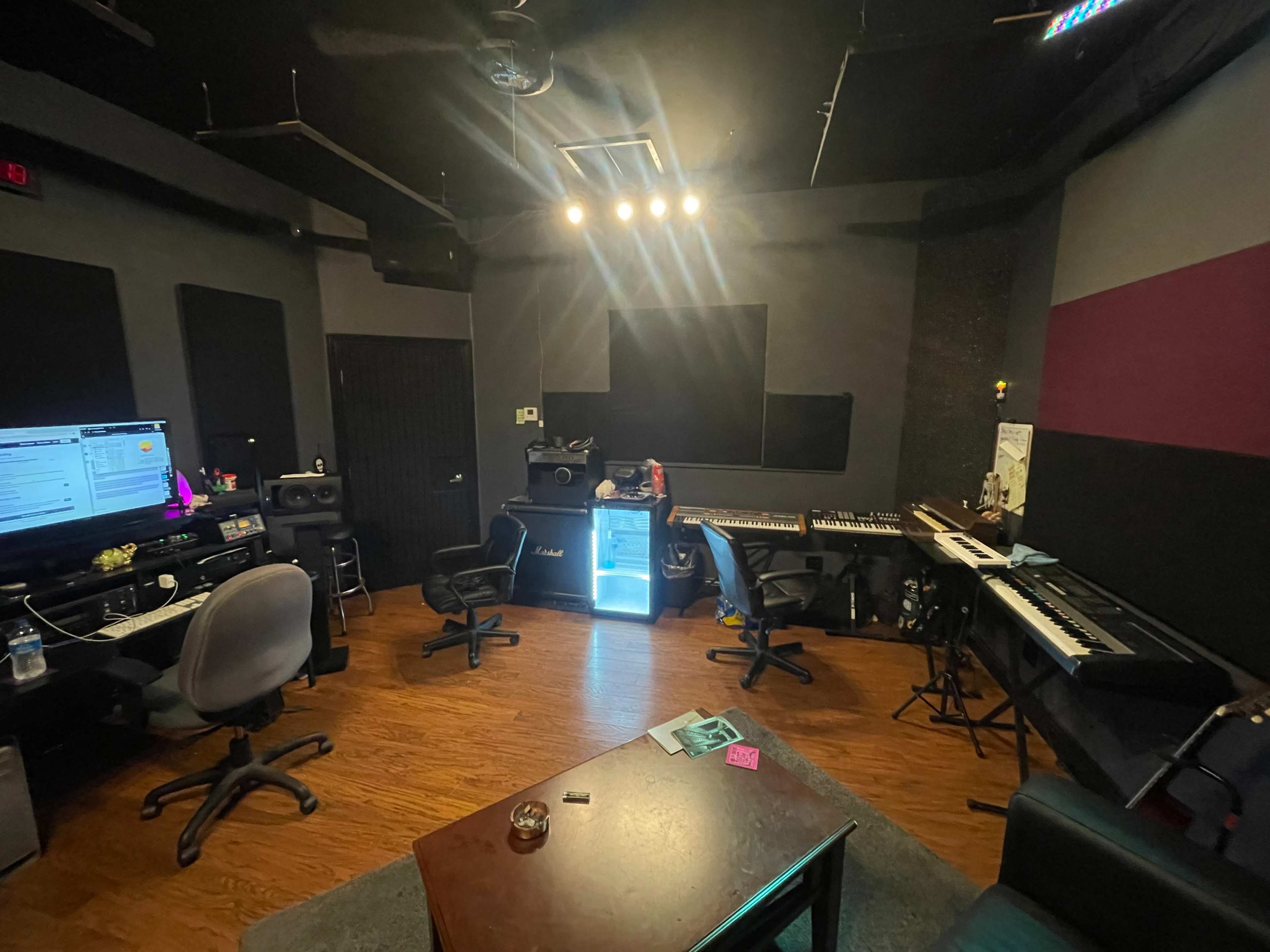 A music production studio featuring a computer setup, keyboards, speakers, and a seating area.