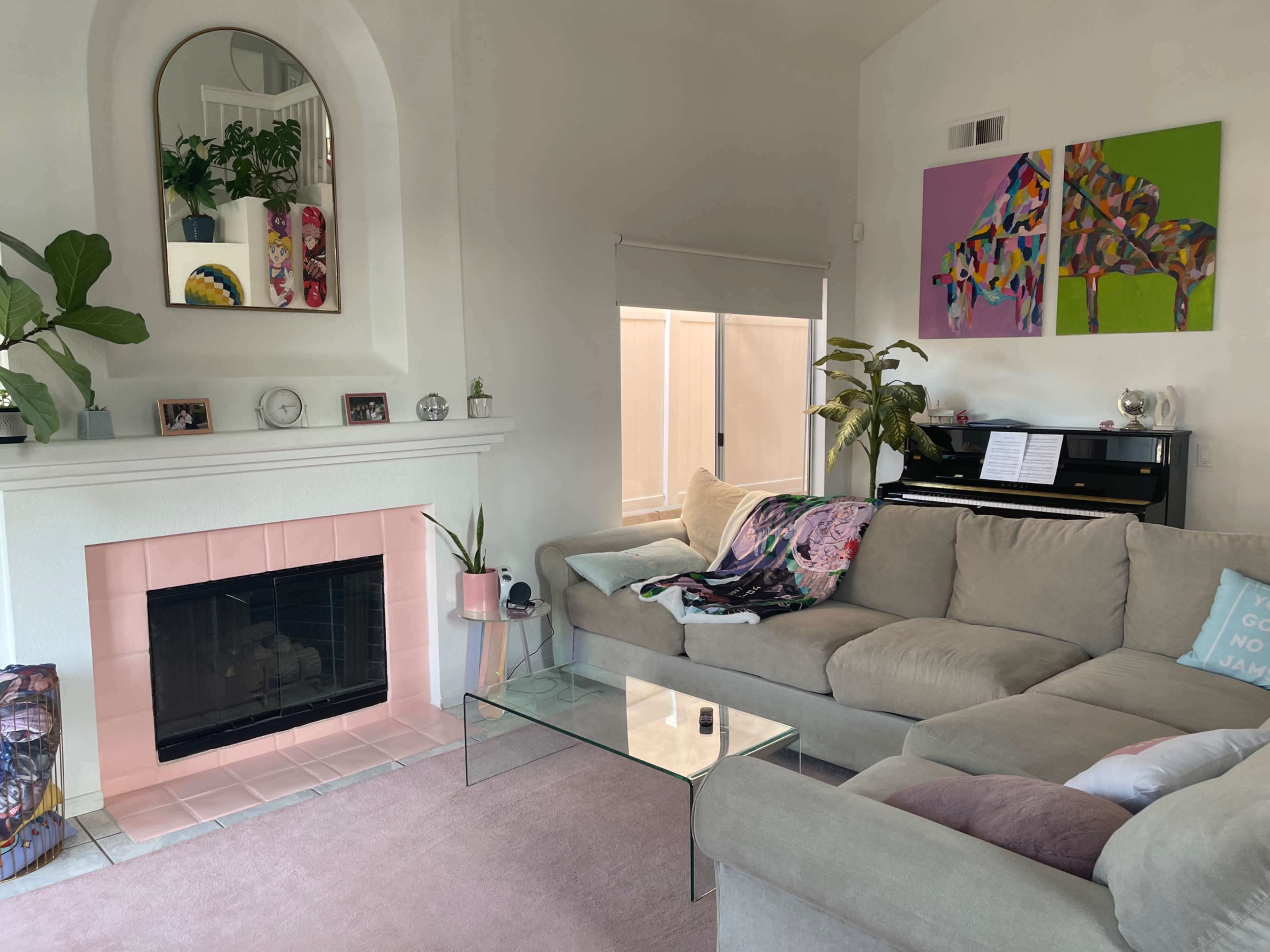 The living room features a light-colored sectional sofa, a glass coffee table, a fireplace with a pink tile surround, and a piano beside large windows.