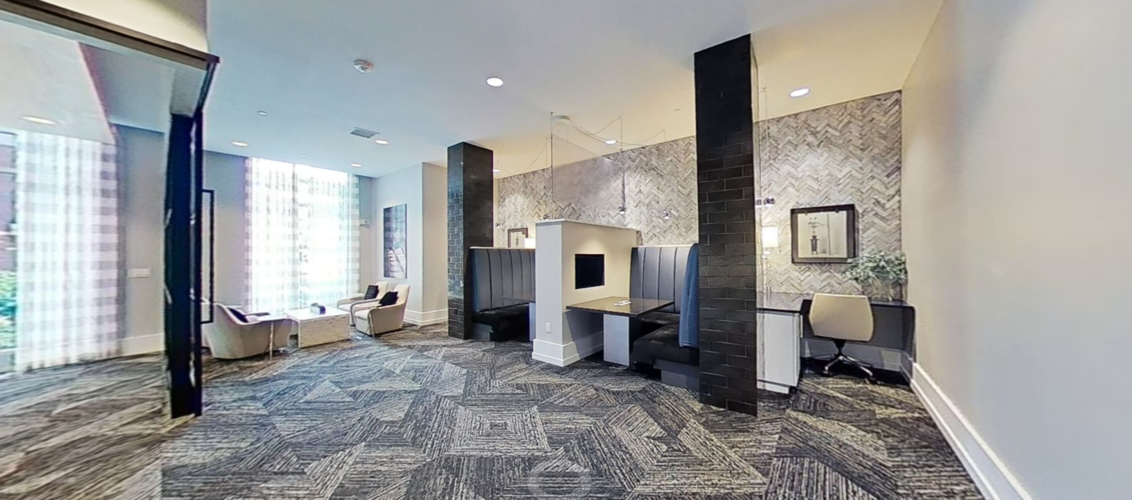 A modern office space featuring two workstations and comfortable seating areas with large windows allowing natural light to enter.