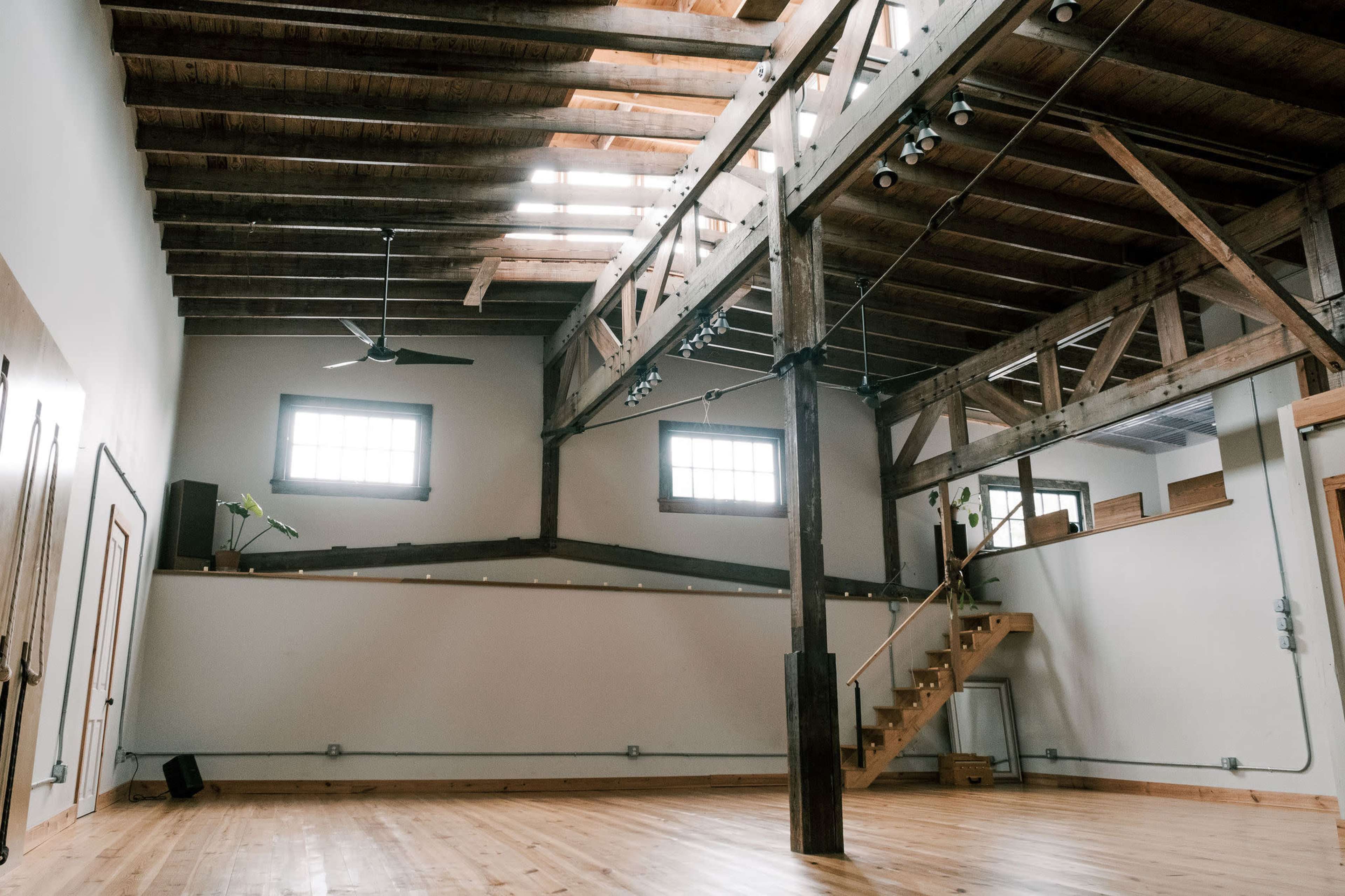 The image shows an interior space with high ceilings, exposed wooden beams, and a staircase leading to an upper level.