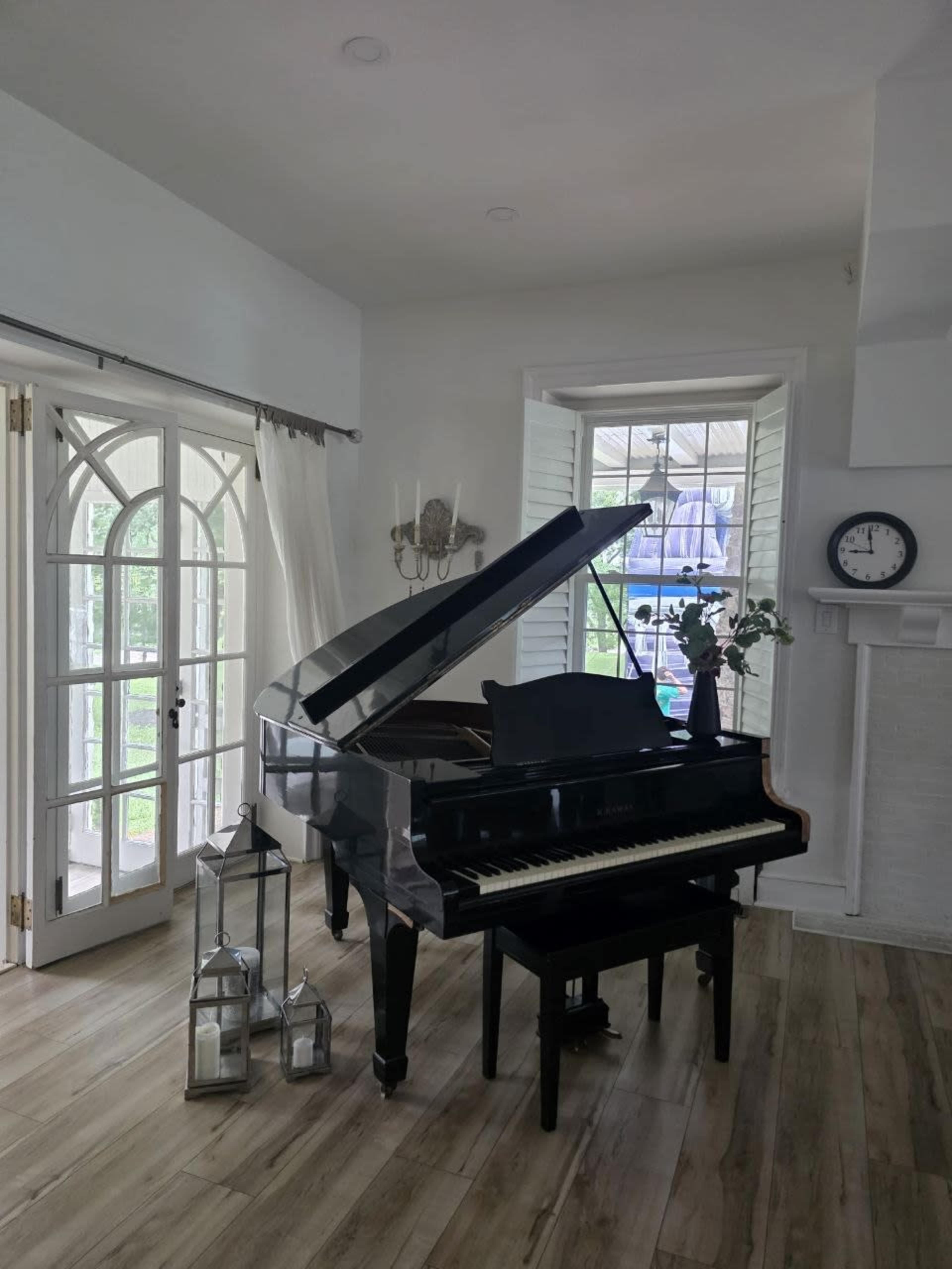 A black grand piano is positioned in a brightly lit room with large windows and wooden flooring.