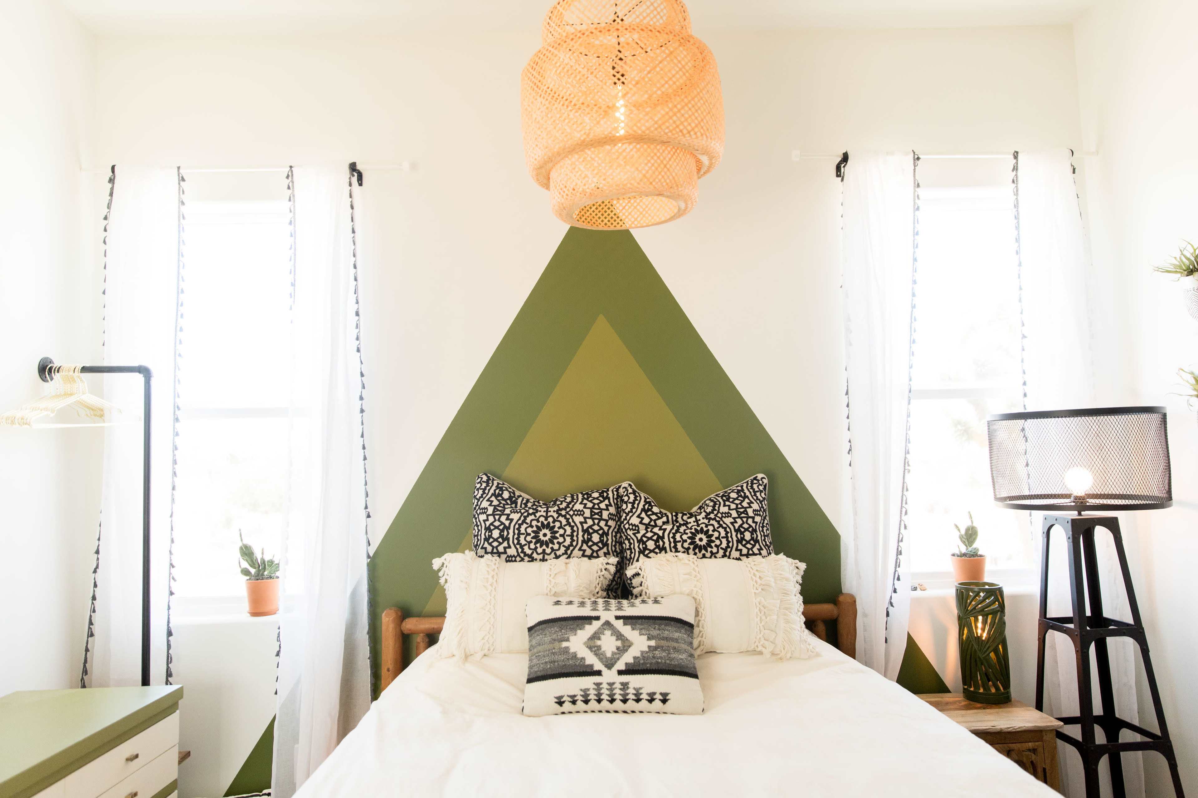 A bedroom features a bed with patterned pillows against a green accent wall, complemented by a pendant light and window treatments.