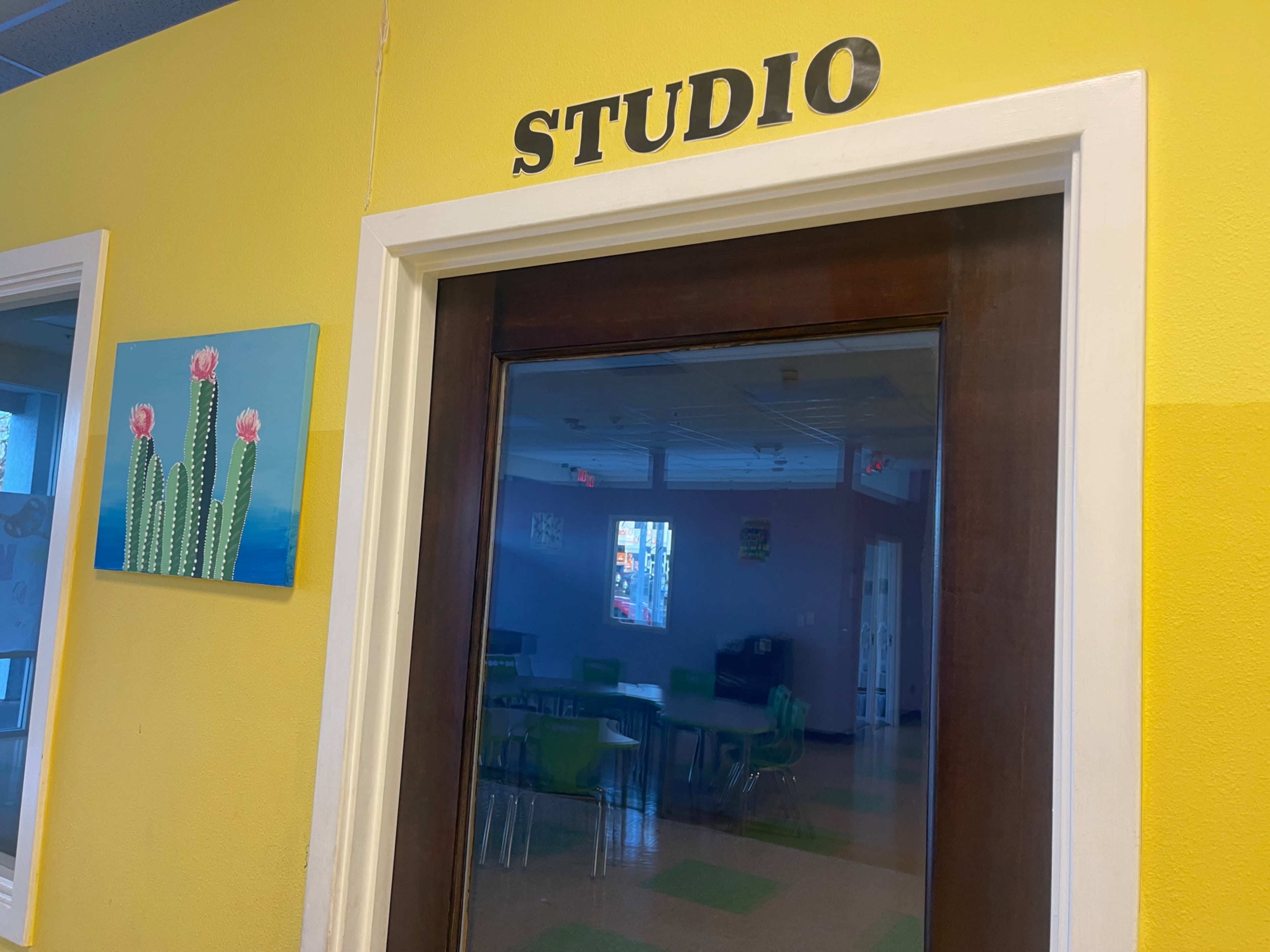 A door with the word "STUDIO" above it leads into a brightly painted space featuring a cactus painting on the wall.